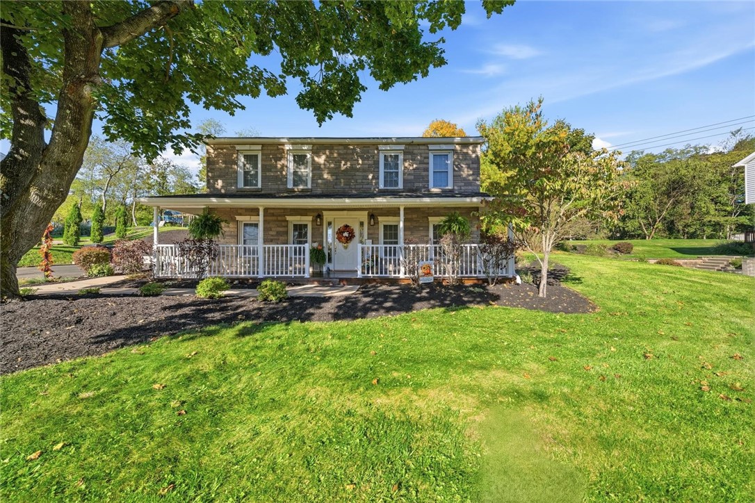 Two-story stone house with a covered front porch, wreath-adorned door, and broad green lawn.
