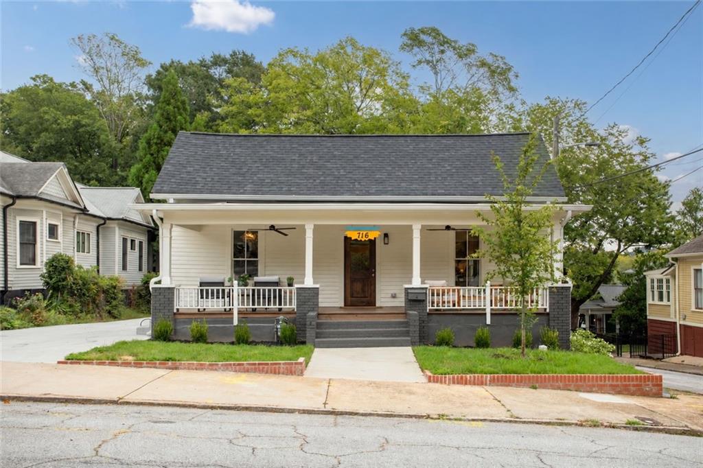 White single-story house with a broad covered porch, dark roof, and the number 716 above its front door.