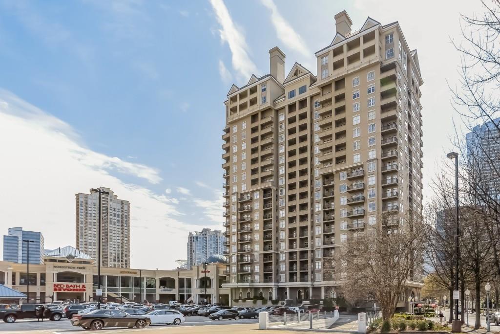 High-rise condominium tower beside a shopping center and parking lot.