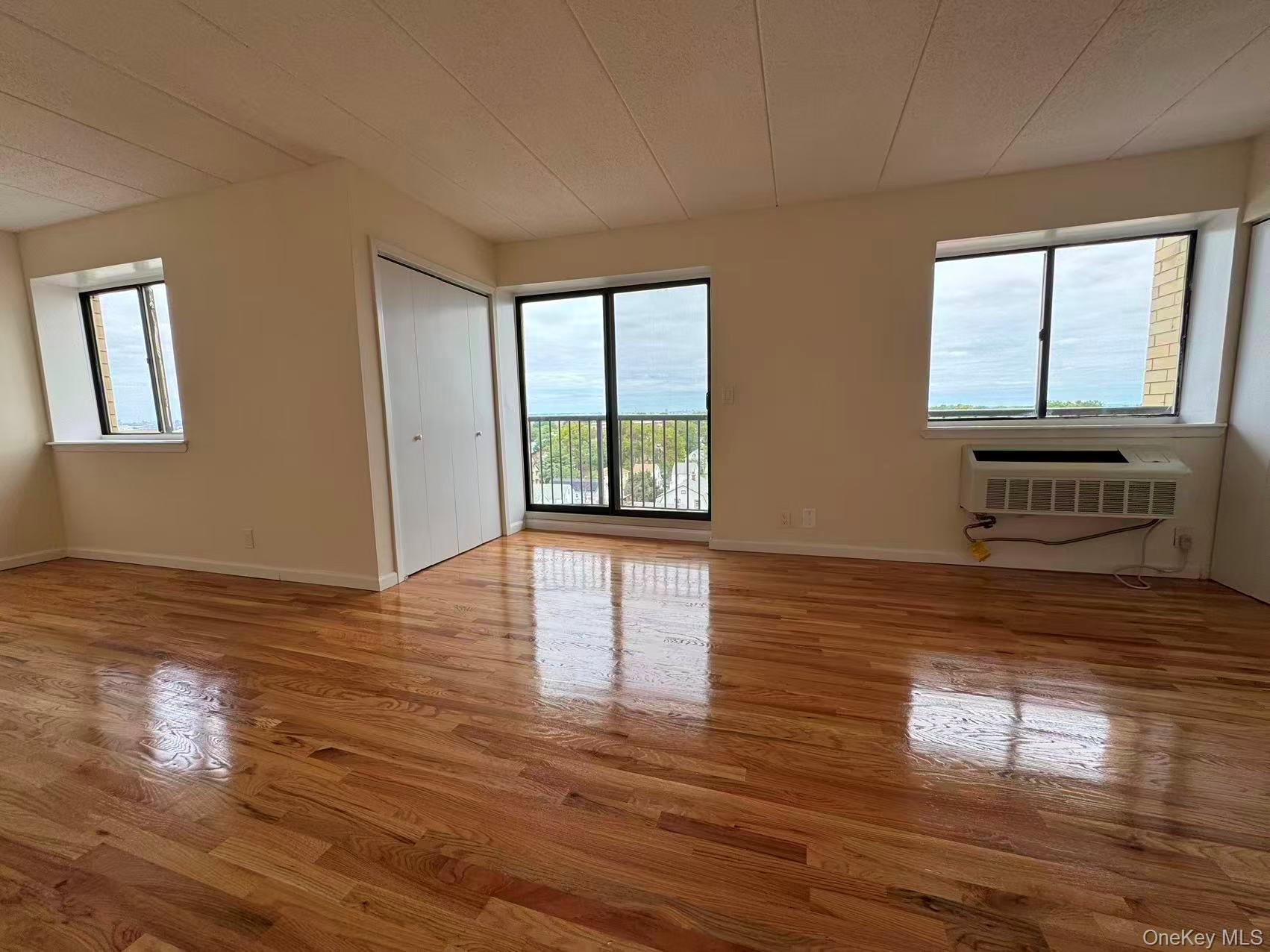 Empty apartment living room with polished hardwood floors, a balcony, and a wall-mounted air conditioner.