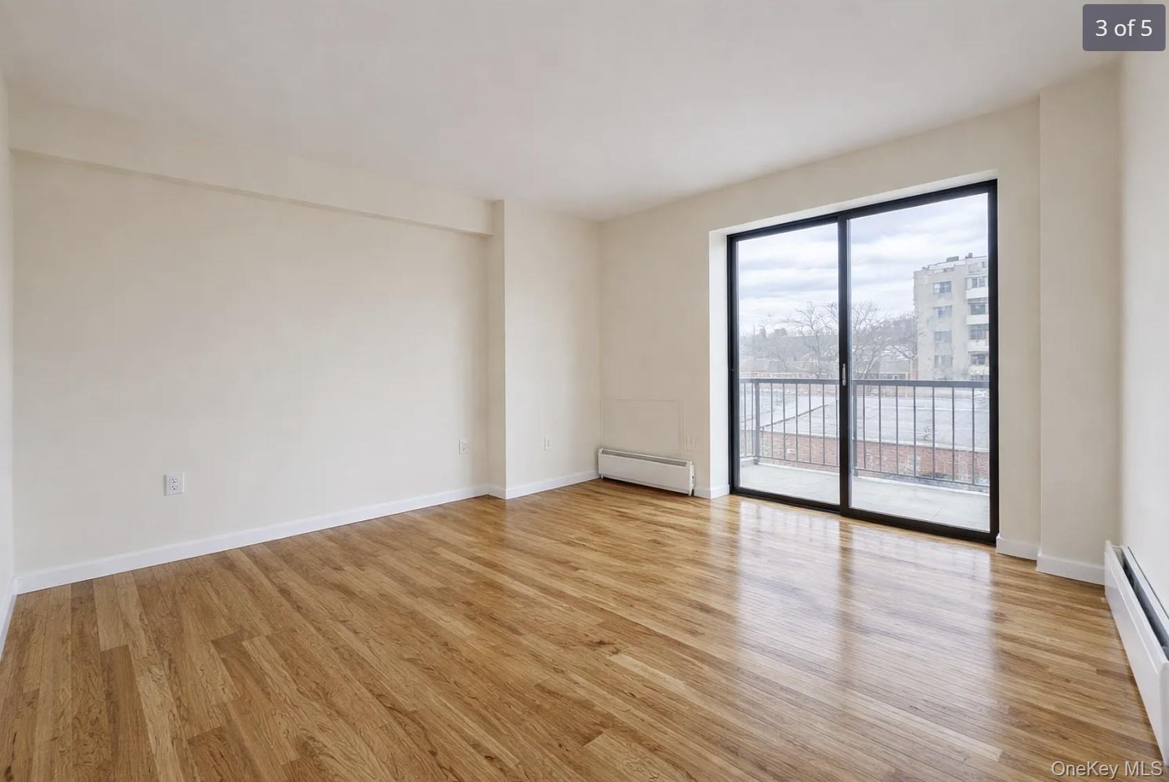 Empty living room with hardwood floors and sliding glass doors to a balcony.