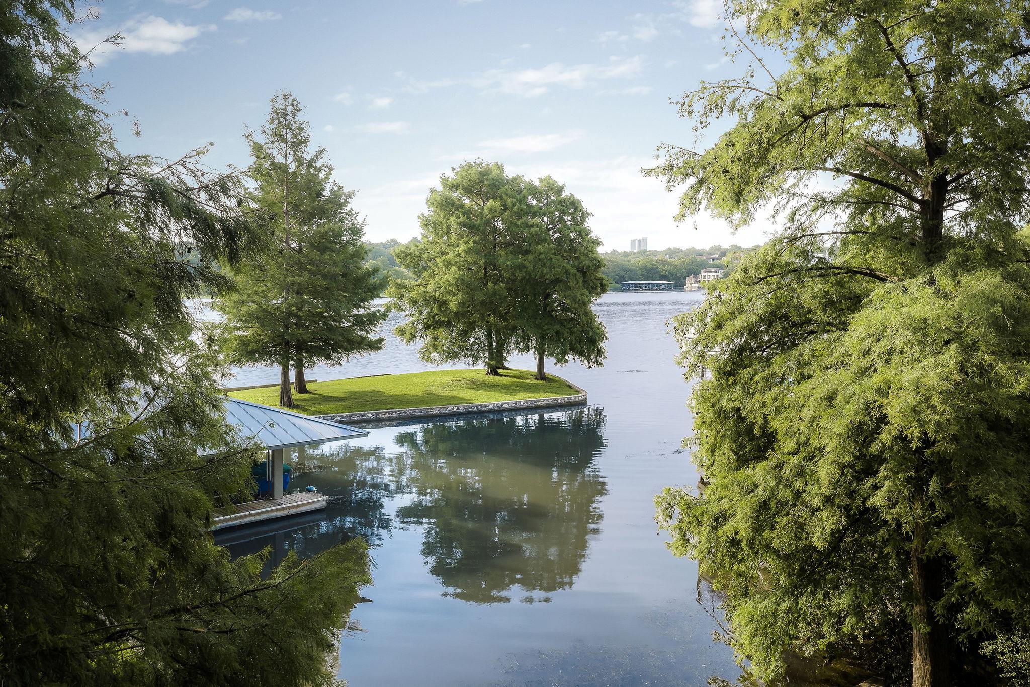 Tree-lined lake with a grassy peninsula and covered boat dock.
