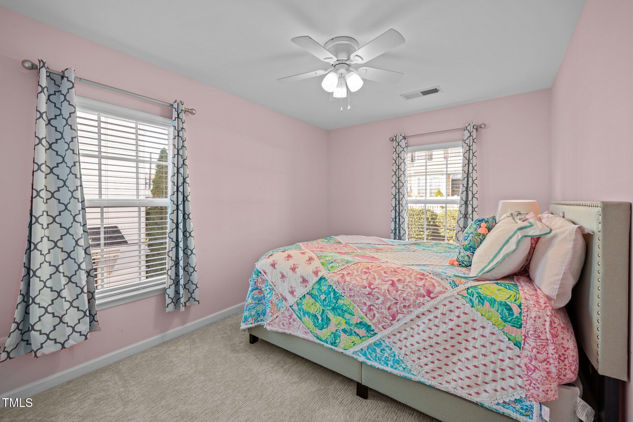 Bedroom with pink walls, a colorful patchwork bedspread, and two windows with patterned curtains.