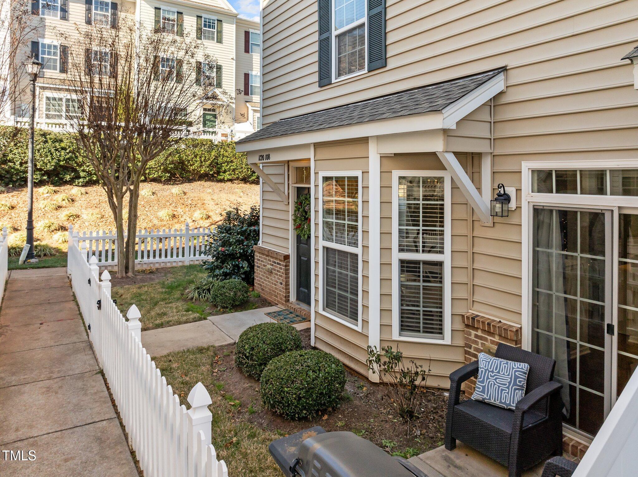Townhouse exterior with a white picket fence enclosing a small courtyard and a chair on the patio.