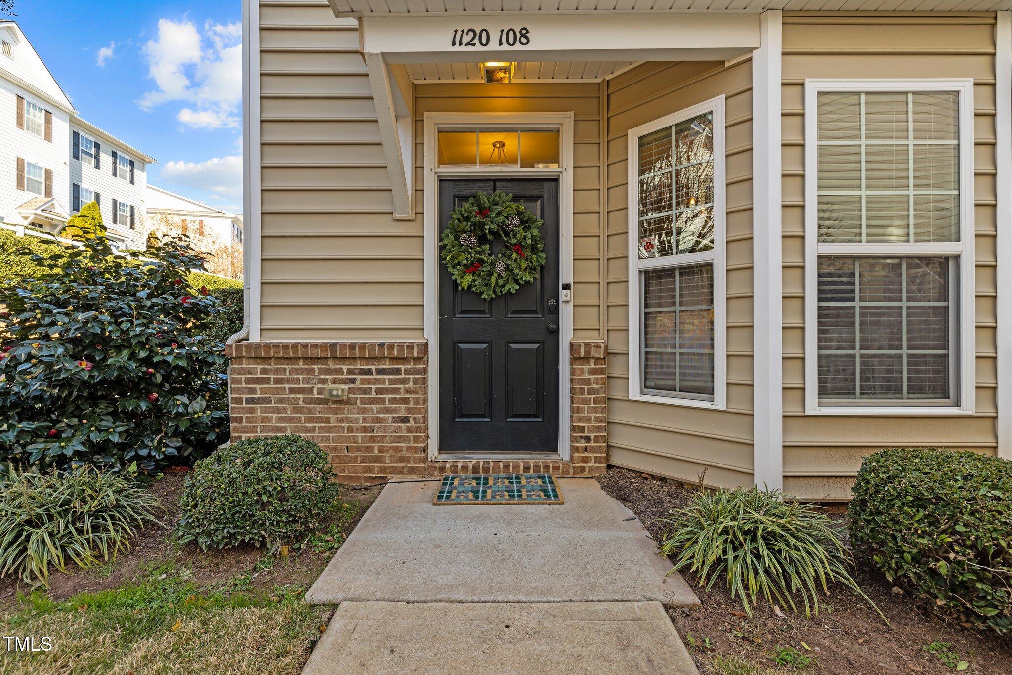 Condo entrance with a black door, holiday wreath, brickwork, and landscaped walkway.