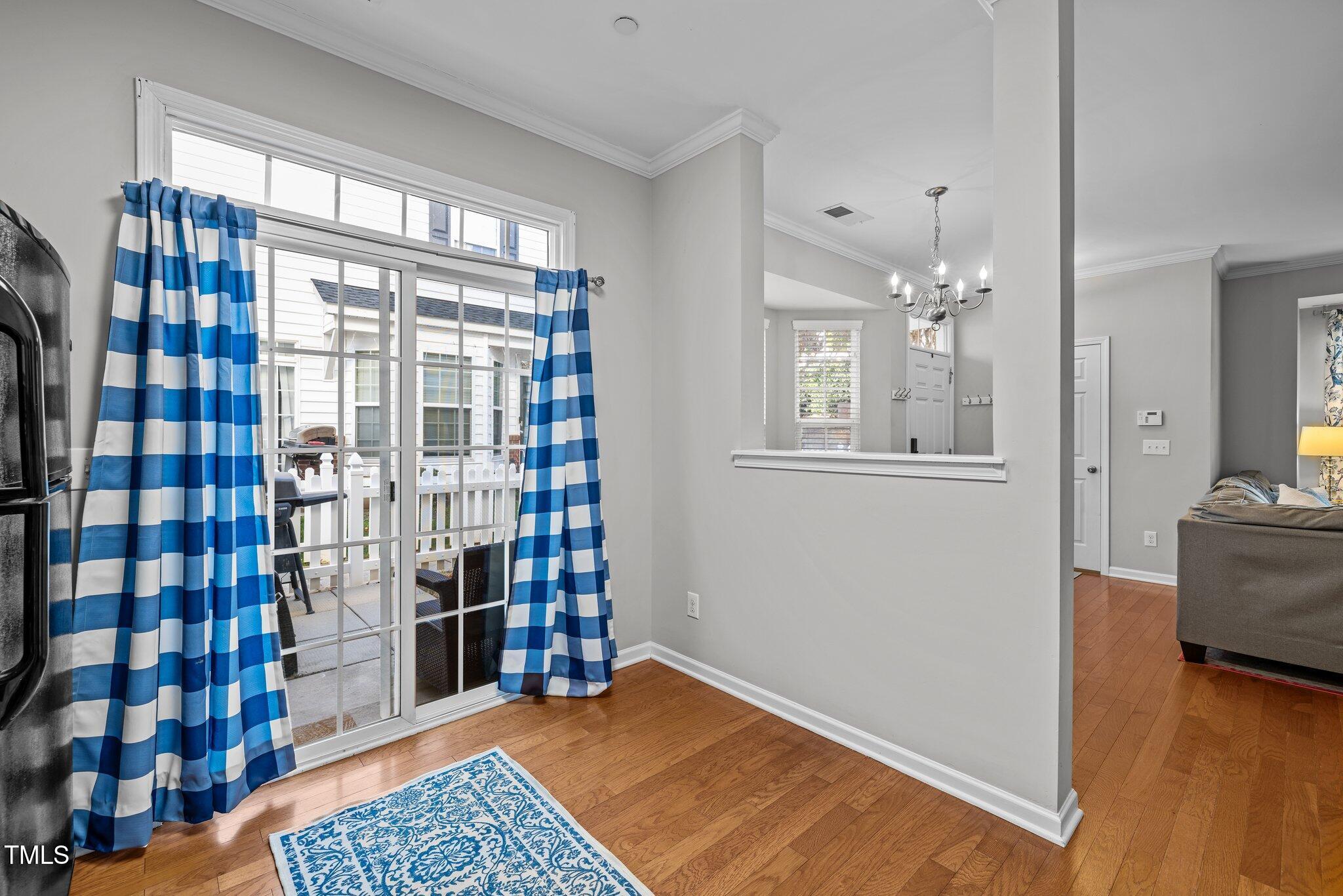 Bright interior with hardwood floors, blue checkered curtains, and a sliding glass door to a fenced patio.