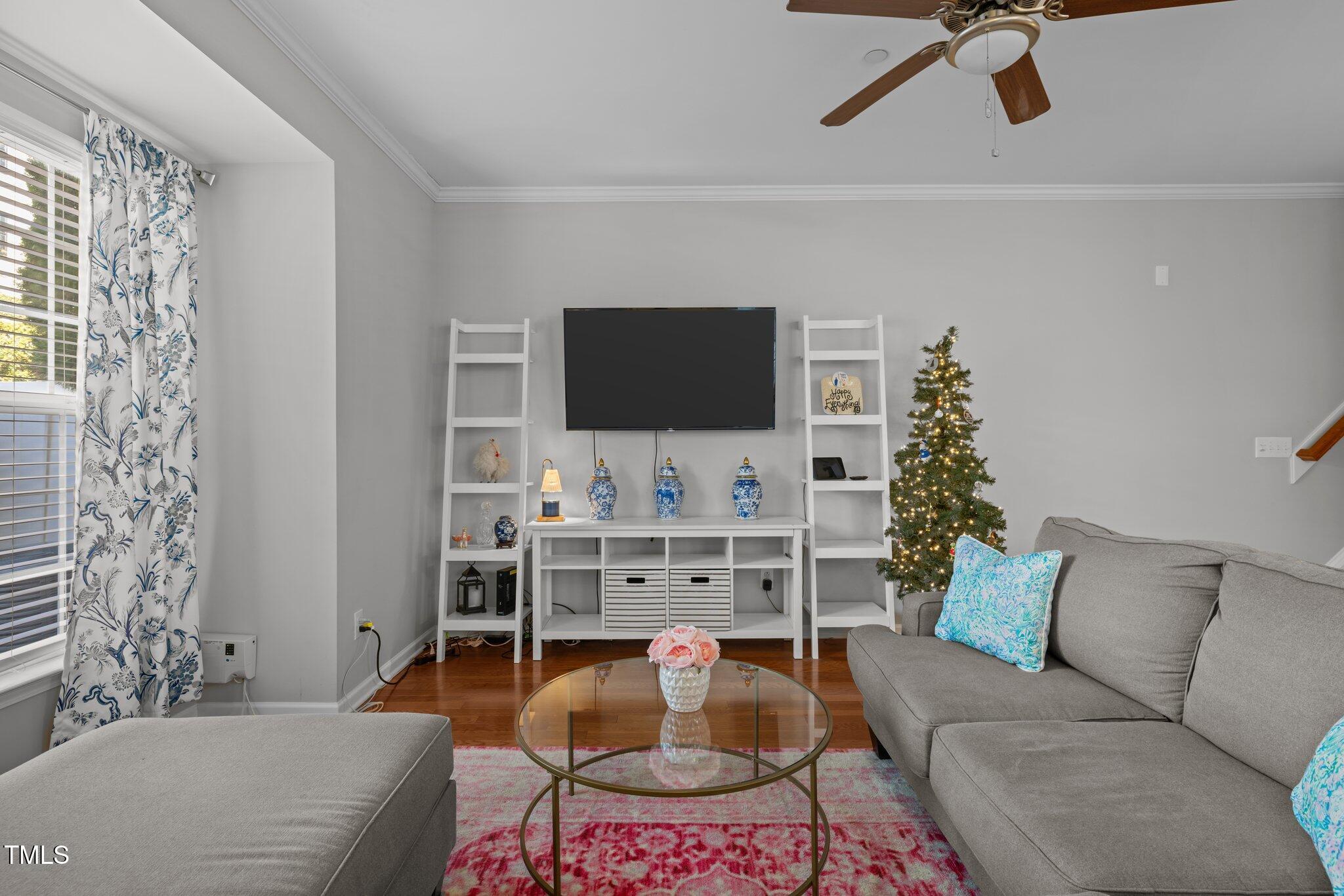 Living room with gray sofas, a glass coffee table, and a lit Christmas tree beside the television.