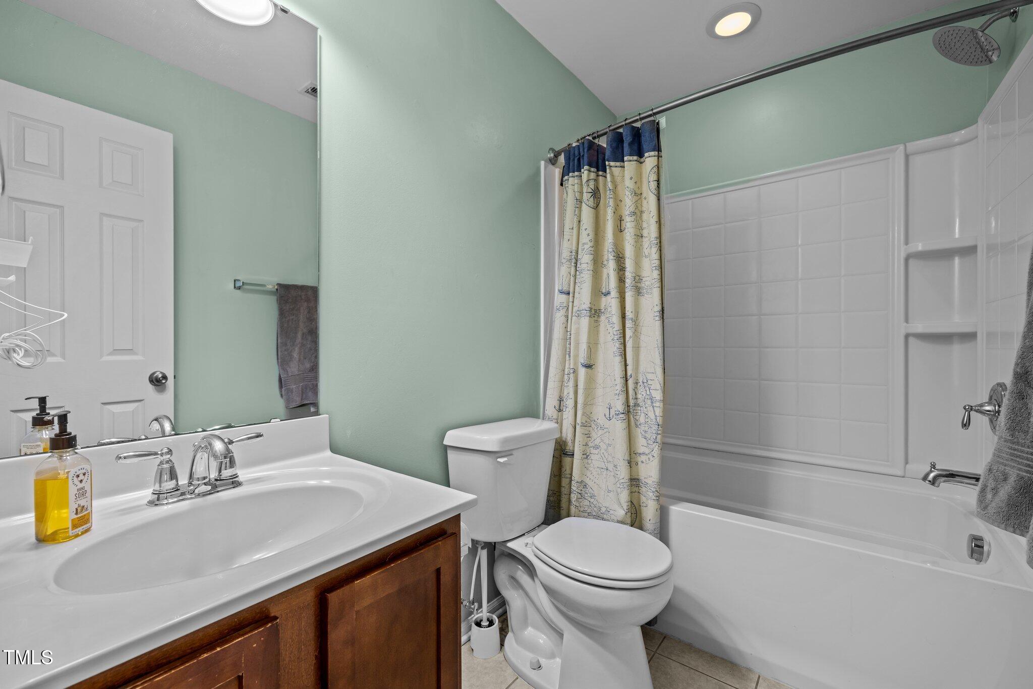Bathroom with a white vanity, toilet, and bathtub behind a map-print shower curtain.