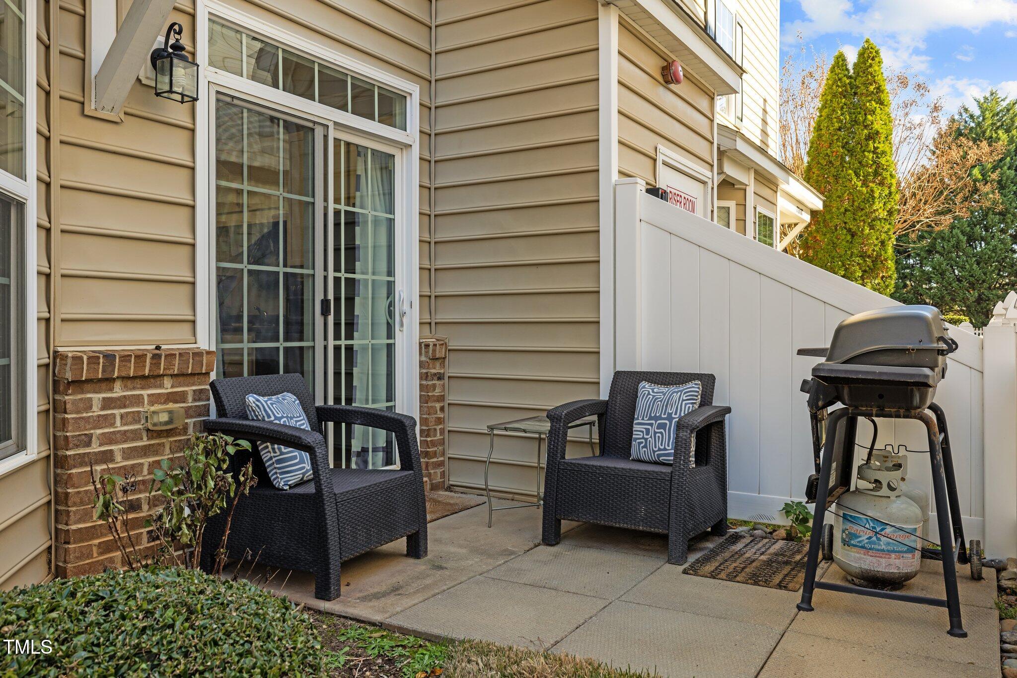 Townhouse patio with two wicker chairs, a sliding glass door, white privacy fence, and propane grill.