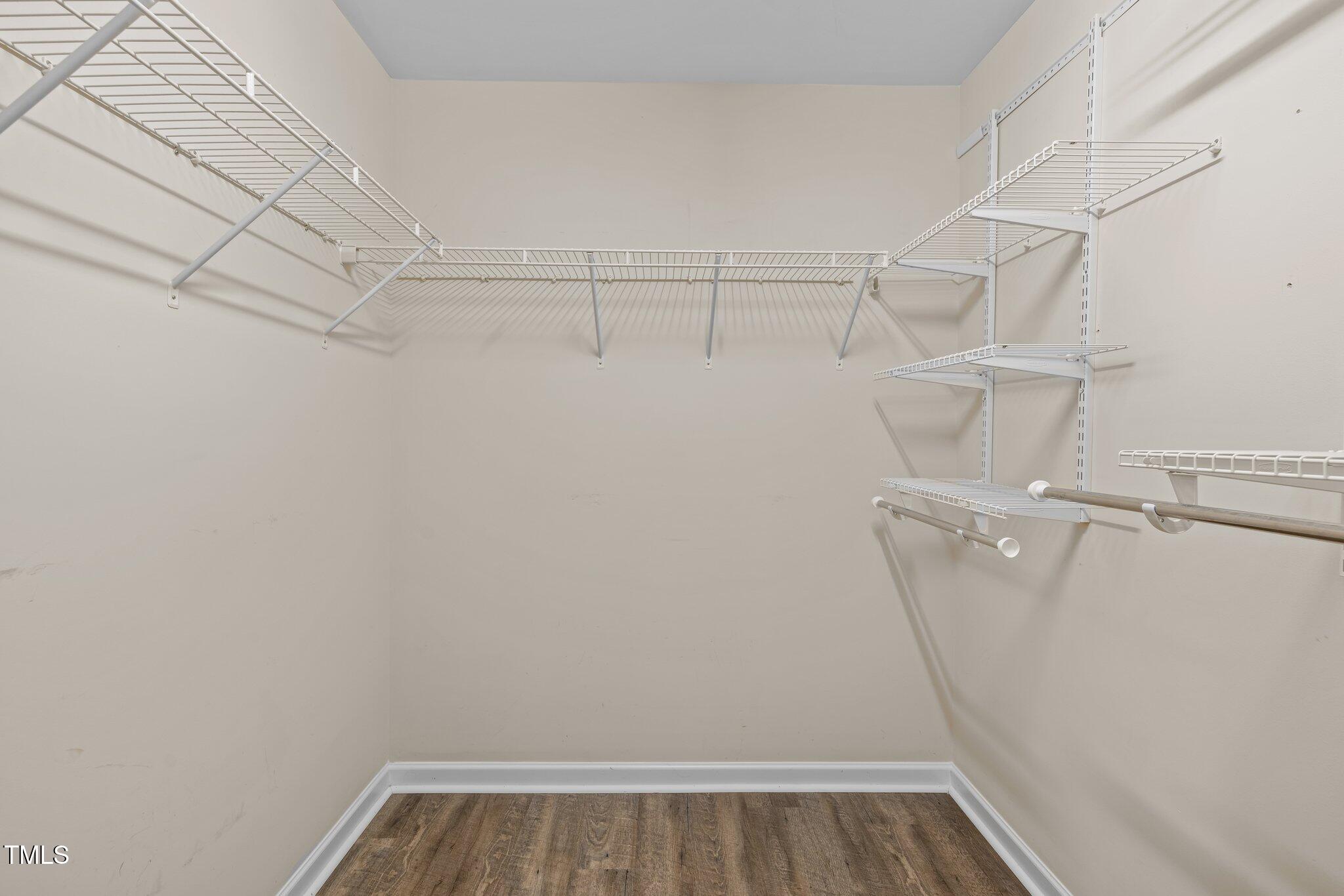 Walk-in closet with white wire shelving on three walls and wood-look flooring.