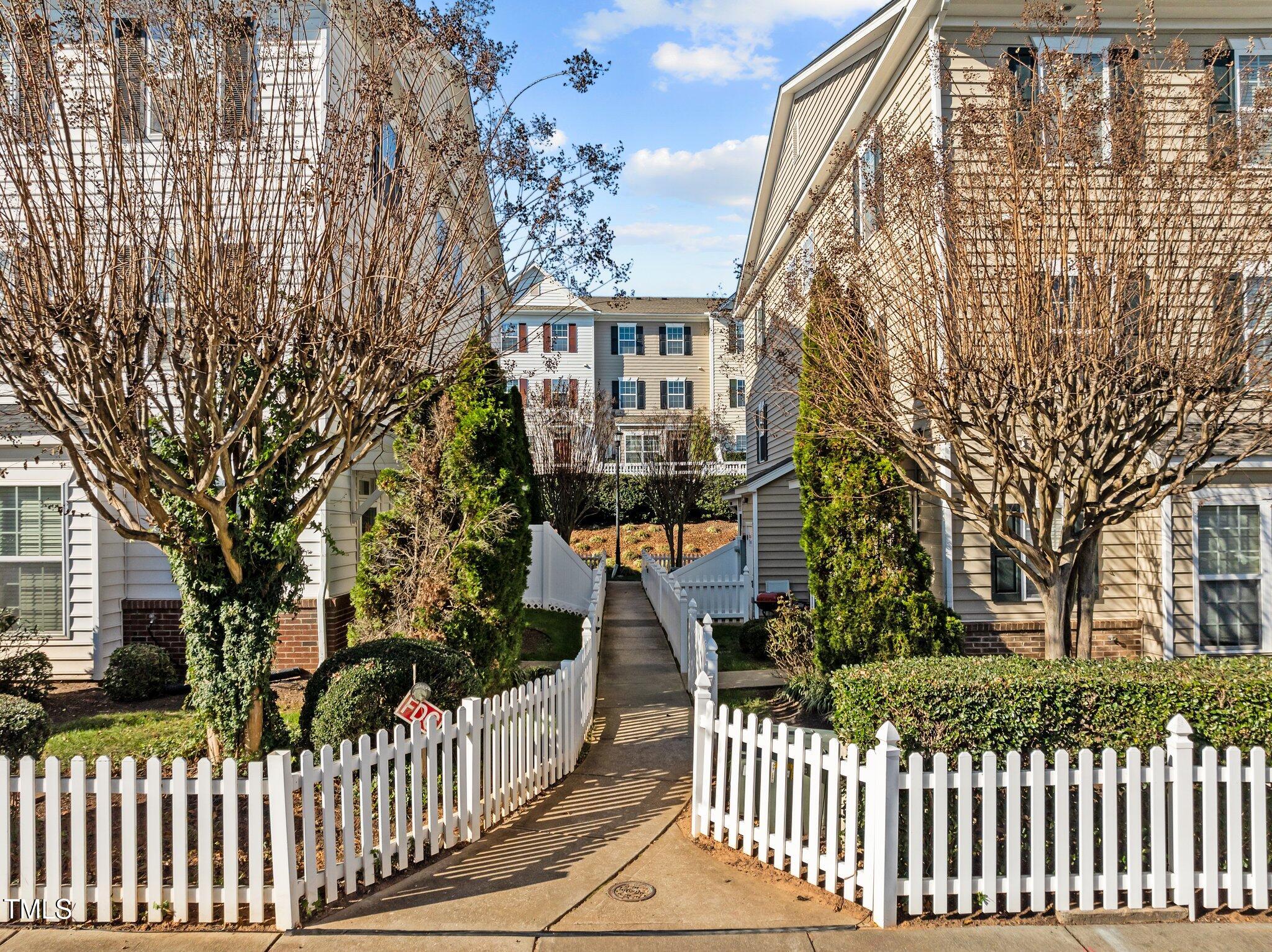 Residential buildings along a walkway bordered by white picket fences and leafless trees.