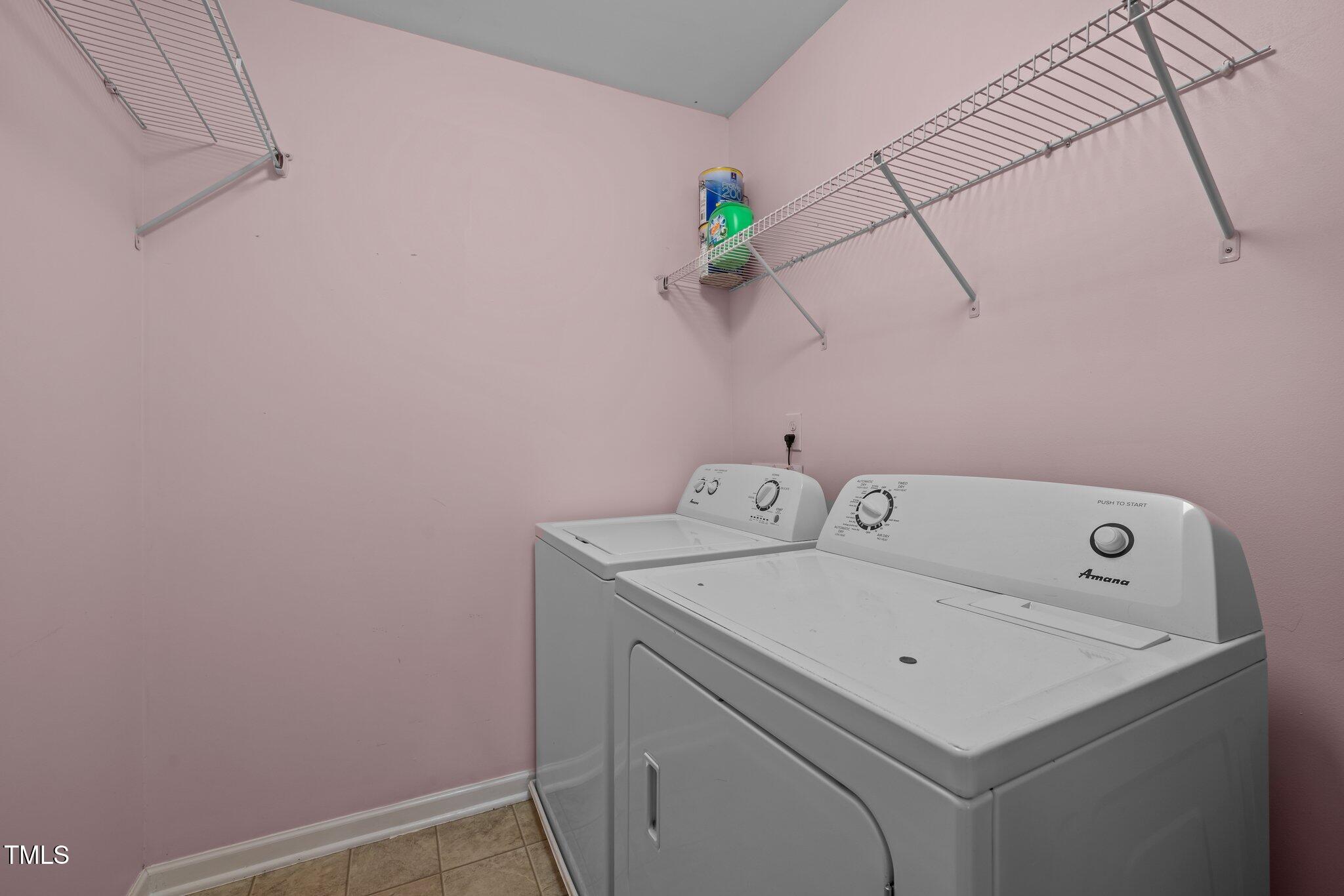 Laundry room with a white washer and dryer beneath wall-mounted wire shelving.