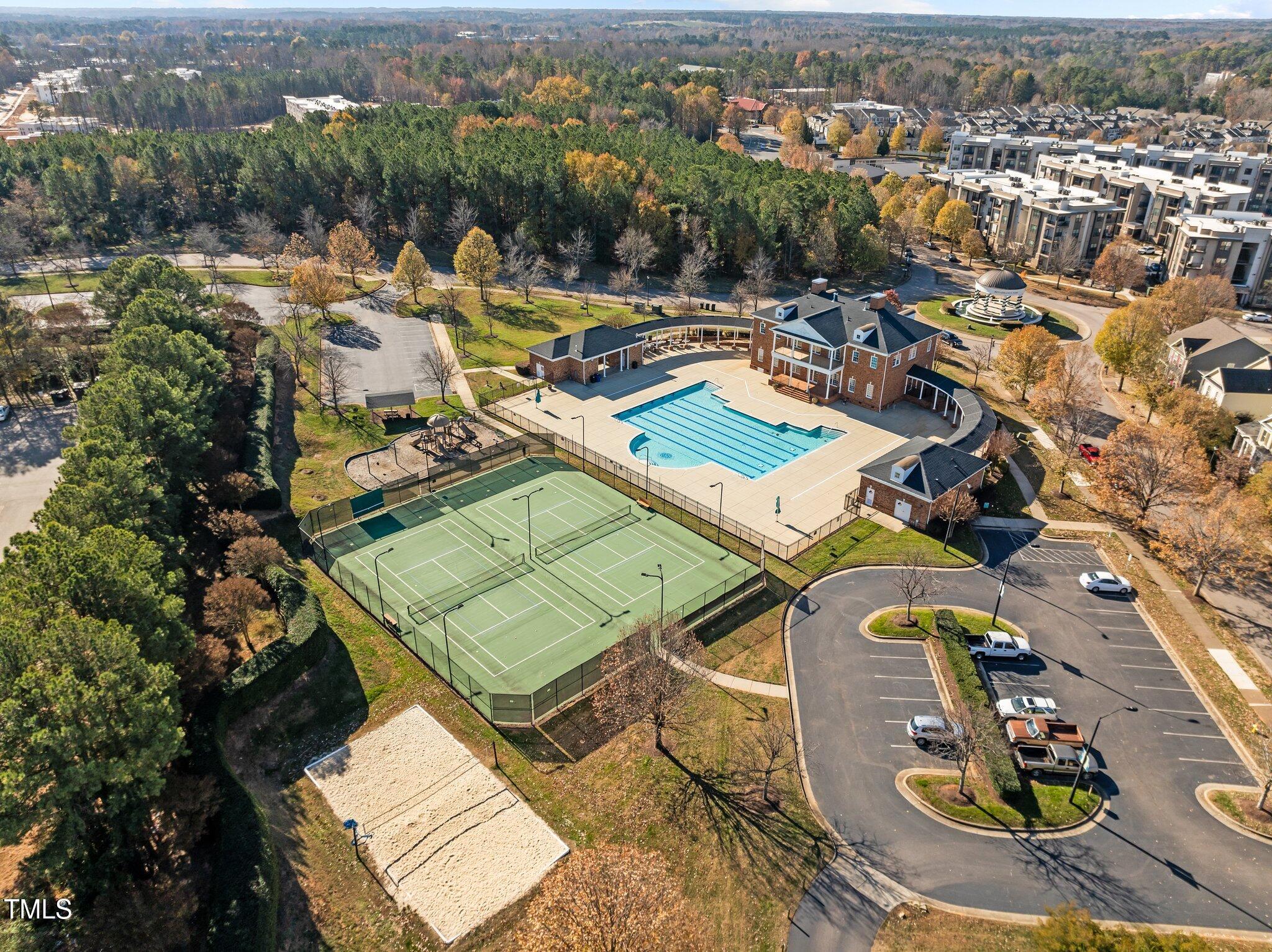 Aerial view of a community pool, tennis courts, clubhouse, playground, and sand volleyball court.