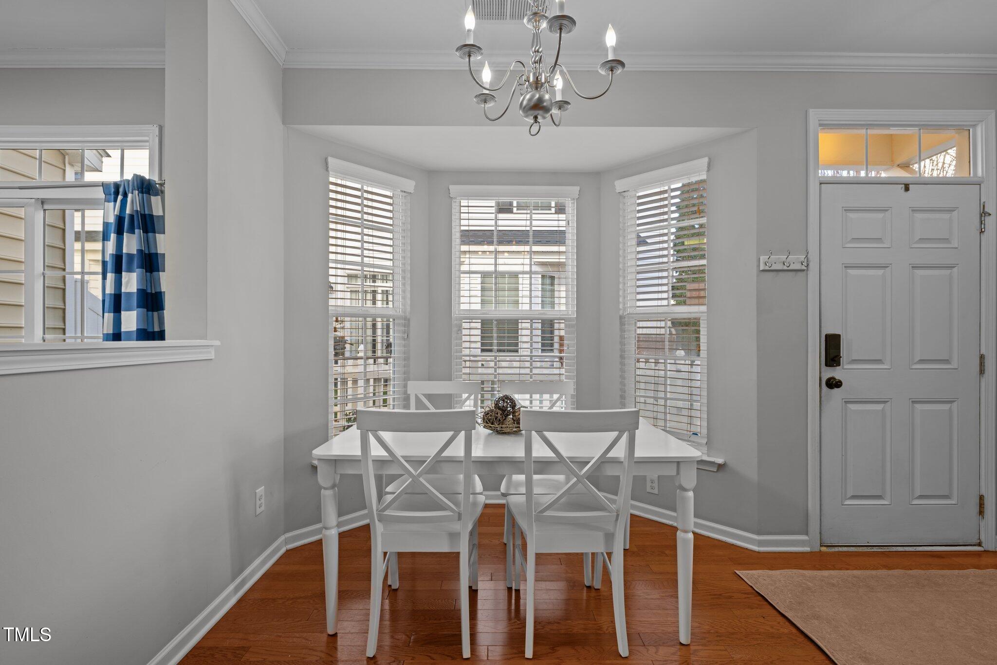 Dining area with a white table and chairs in front of three bay windows.