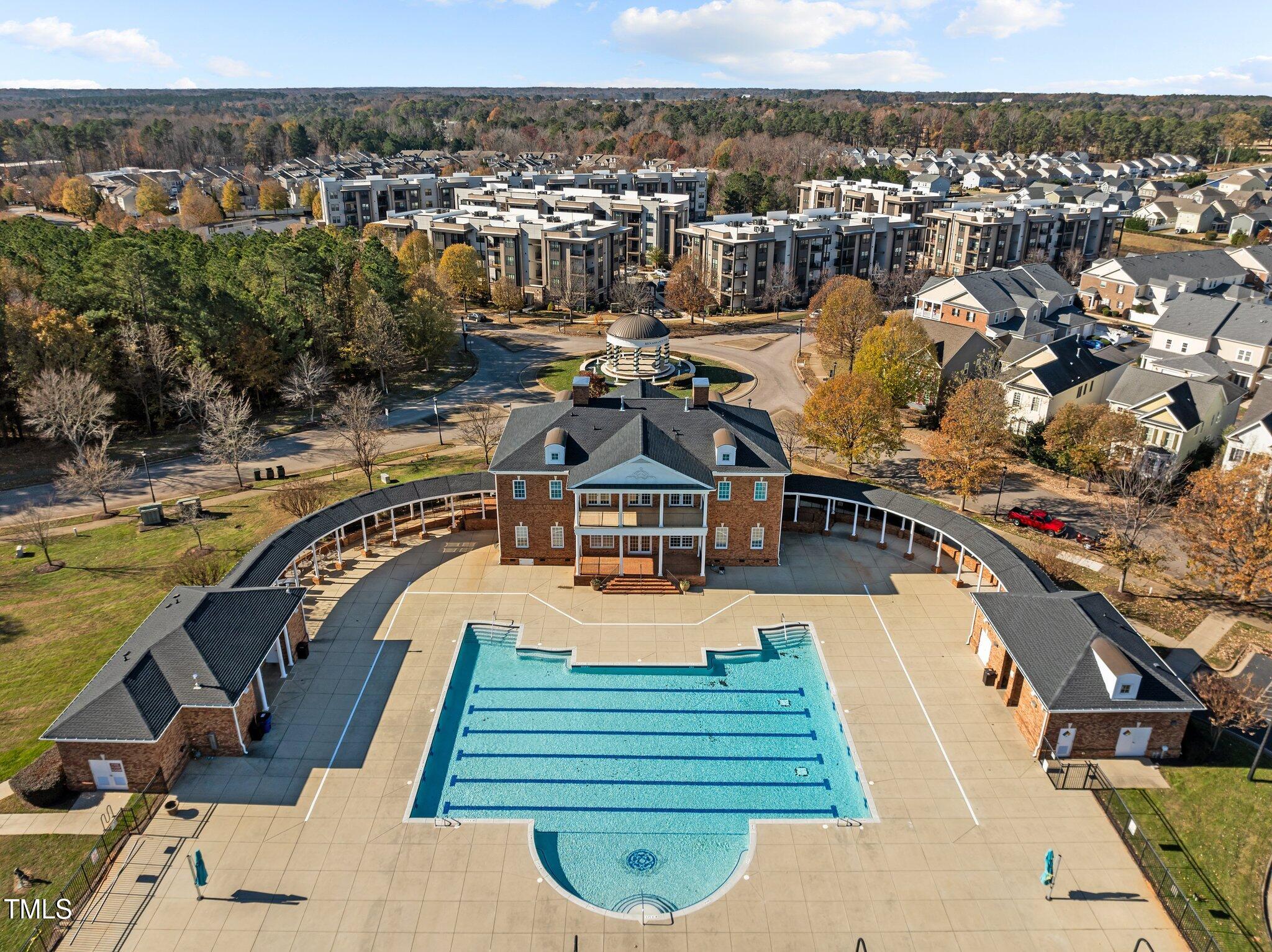 Community swimming pool with lap lanes and rounded shallow end, surrounded by apartments and a clubhouse.