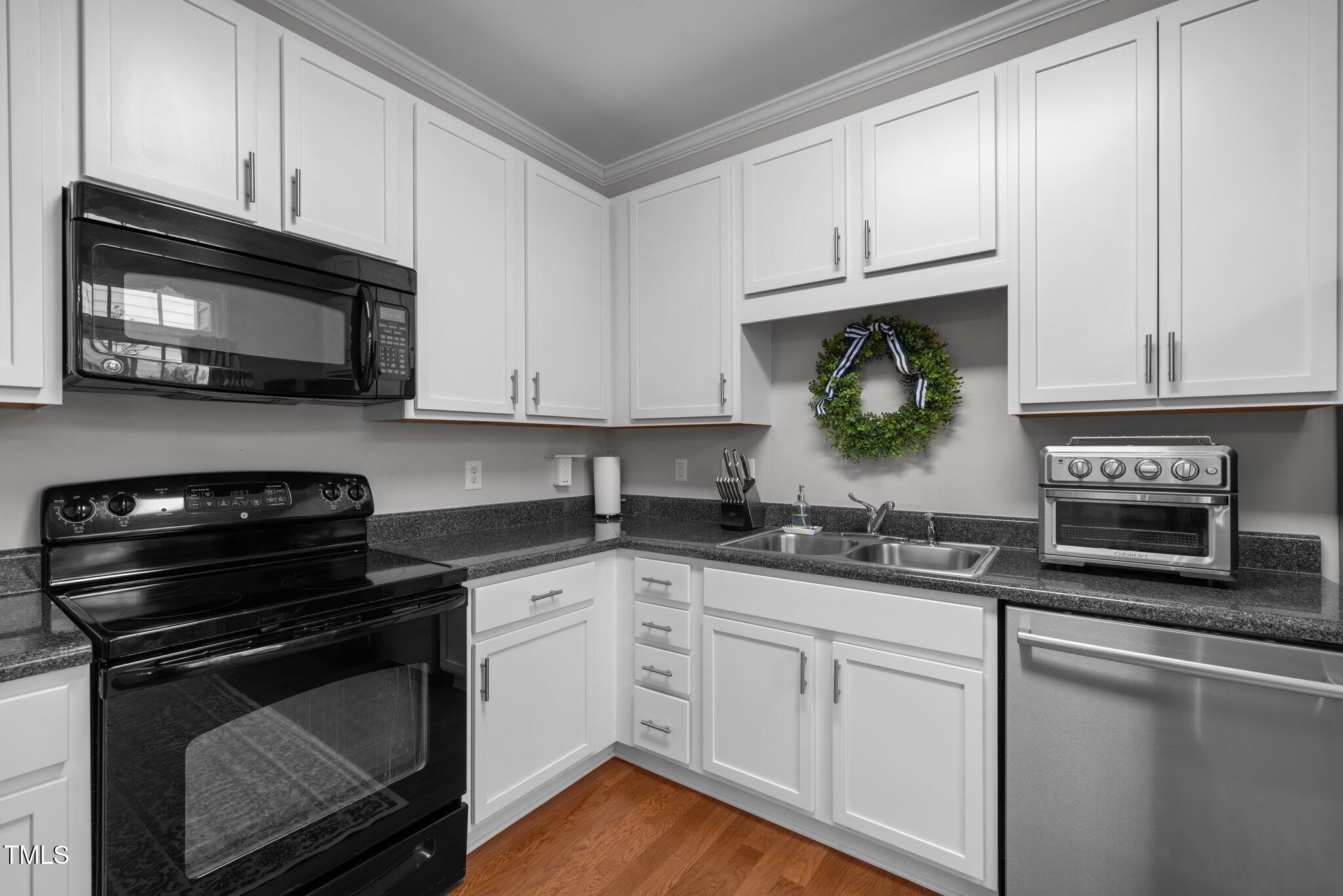 Kitchen with white cabinetry, dark countertops, black range, and stainless-steel dishwasher.