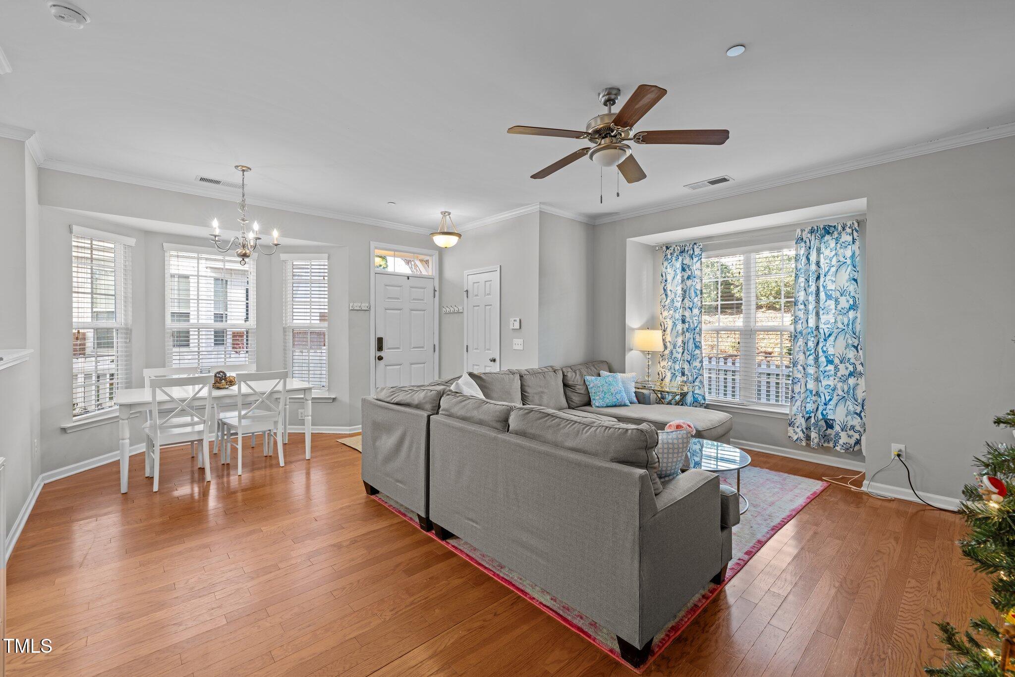 Open-plan living and dining room with a gray sectional, hardwood floors, and large curtained windows.