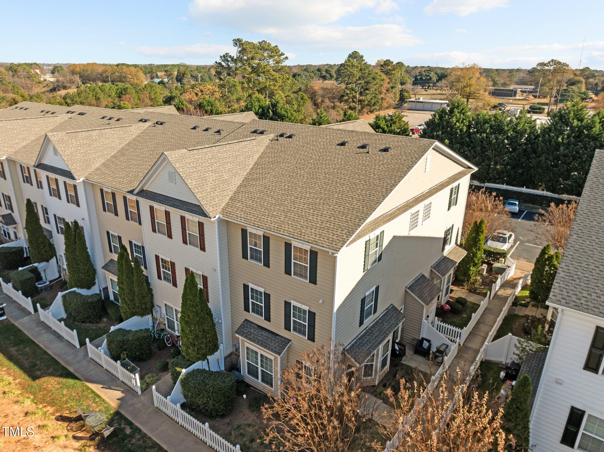Aerial view of beige townhouses with gabled roofs, fenced yards, and a parking area.