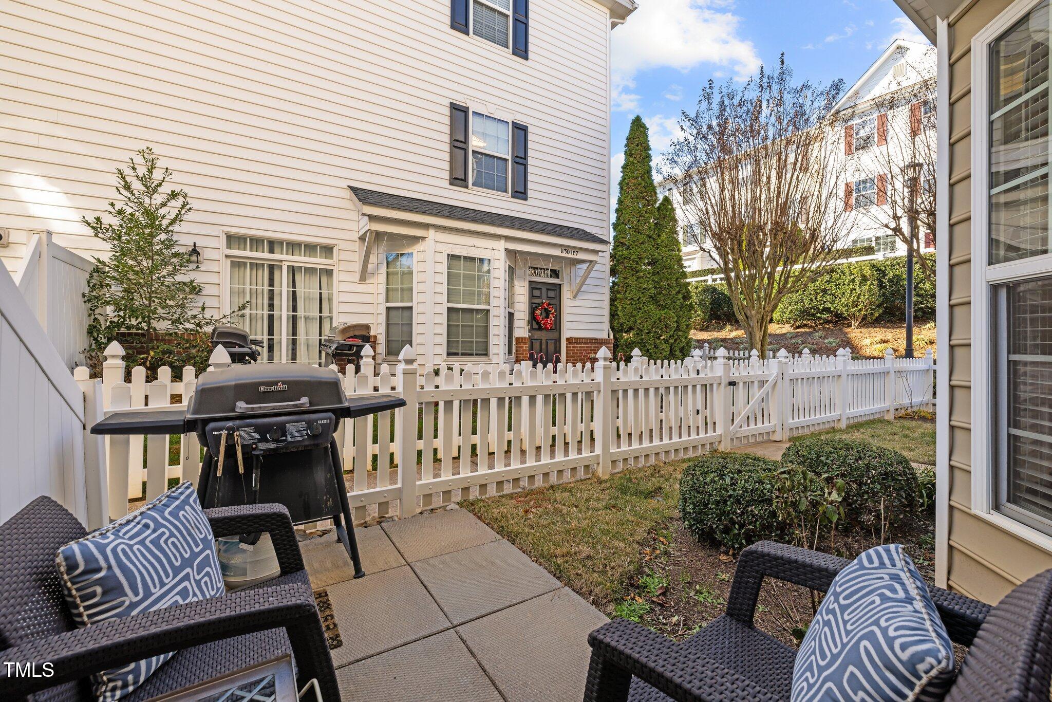 Fenced townhouse patio with wicker chairs, a grill, and a paved walkway.