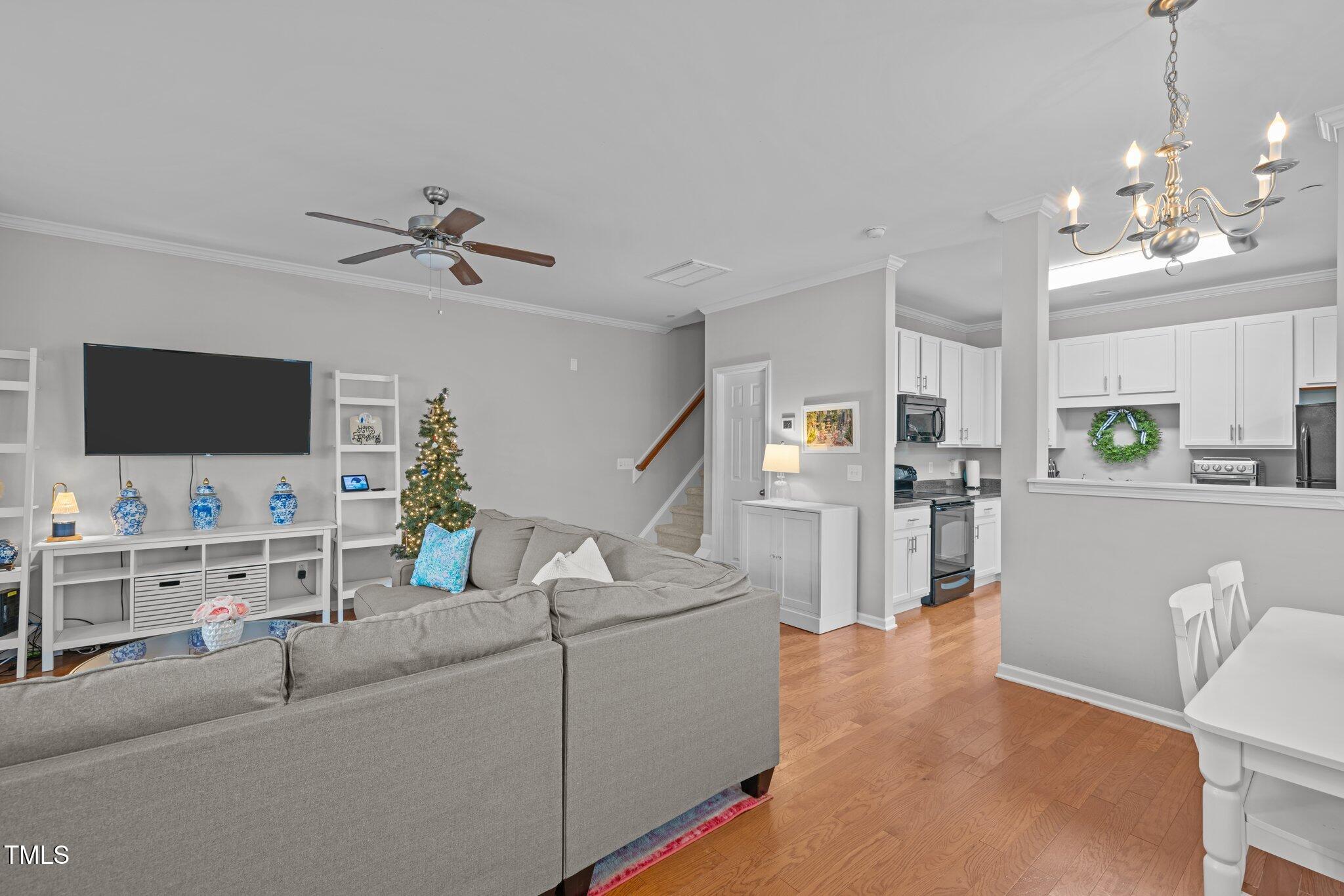 Open-plan living room and kitchen with a gray sectional, hardwood floors, and a decorated Christmas tree.