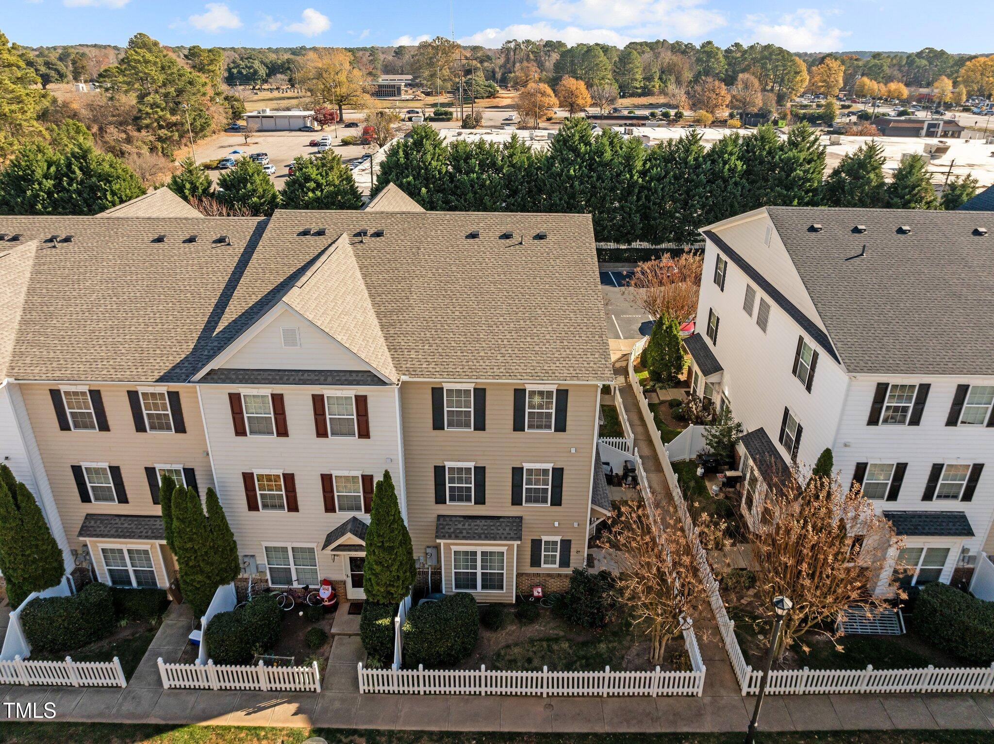 Aerial view of attached beige and white townhomes with fenced yards and autumn trees behind them.
