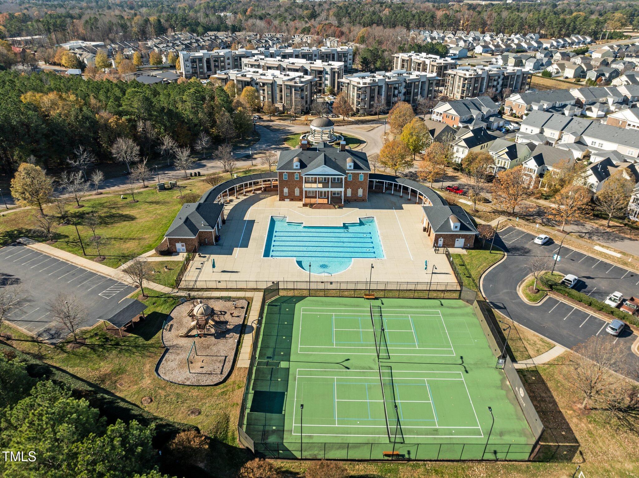 Aerial view of a residential community with a pool, tennis courts, and clubhouse.