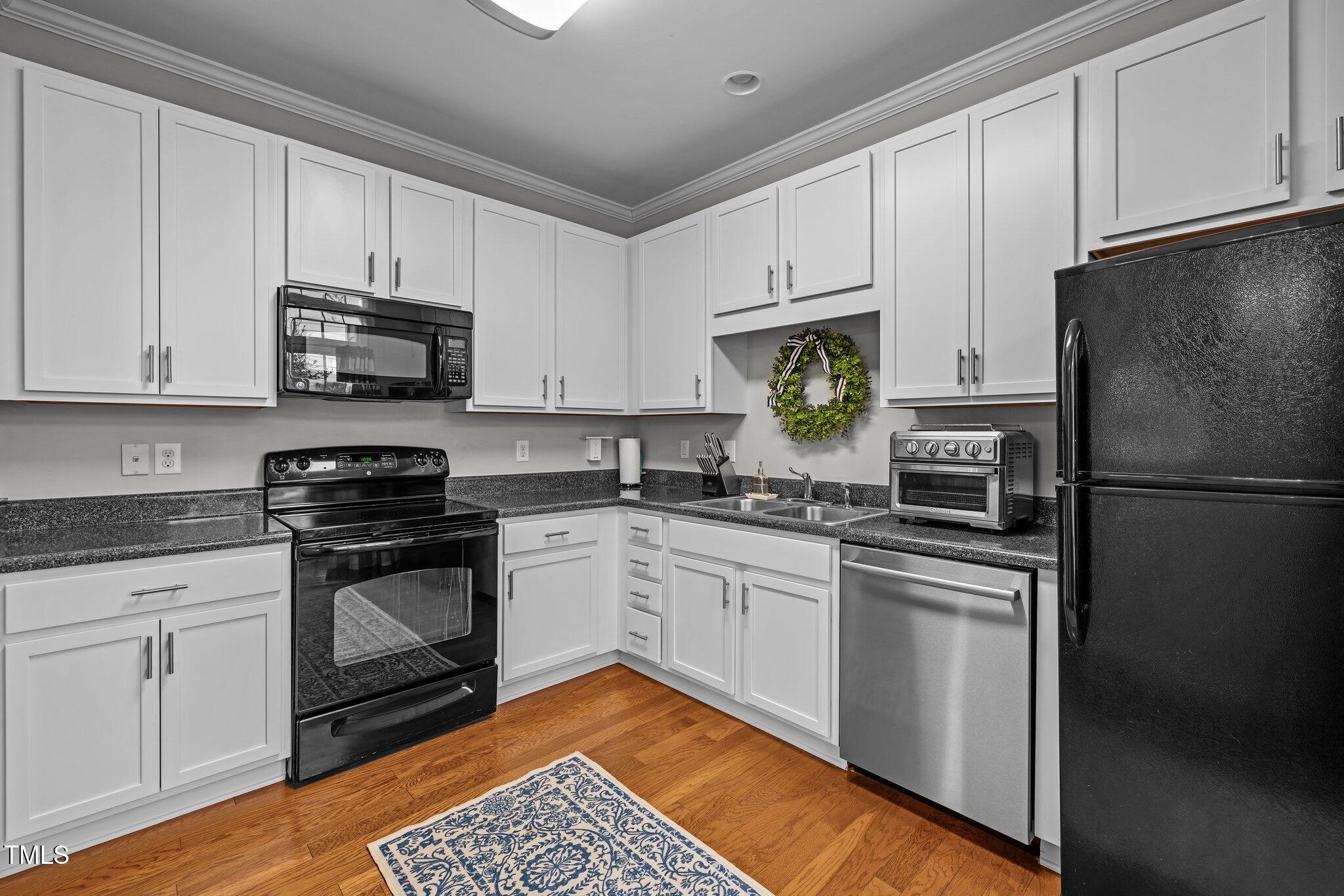 Kitchen with white cabinets, dark countertops, mixed-finish appliances, and hardwood flooring.