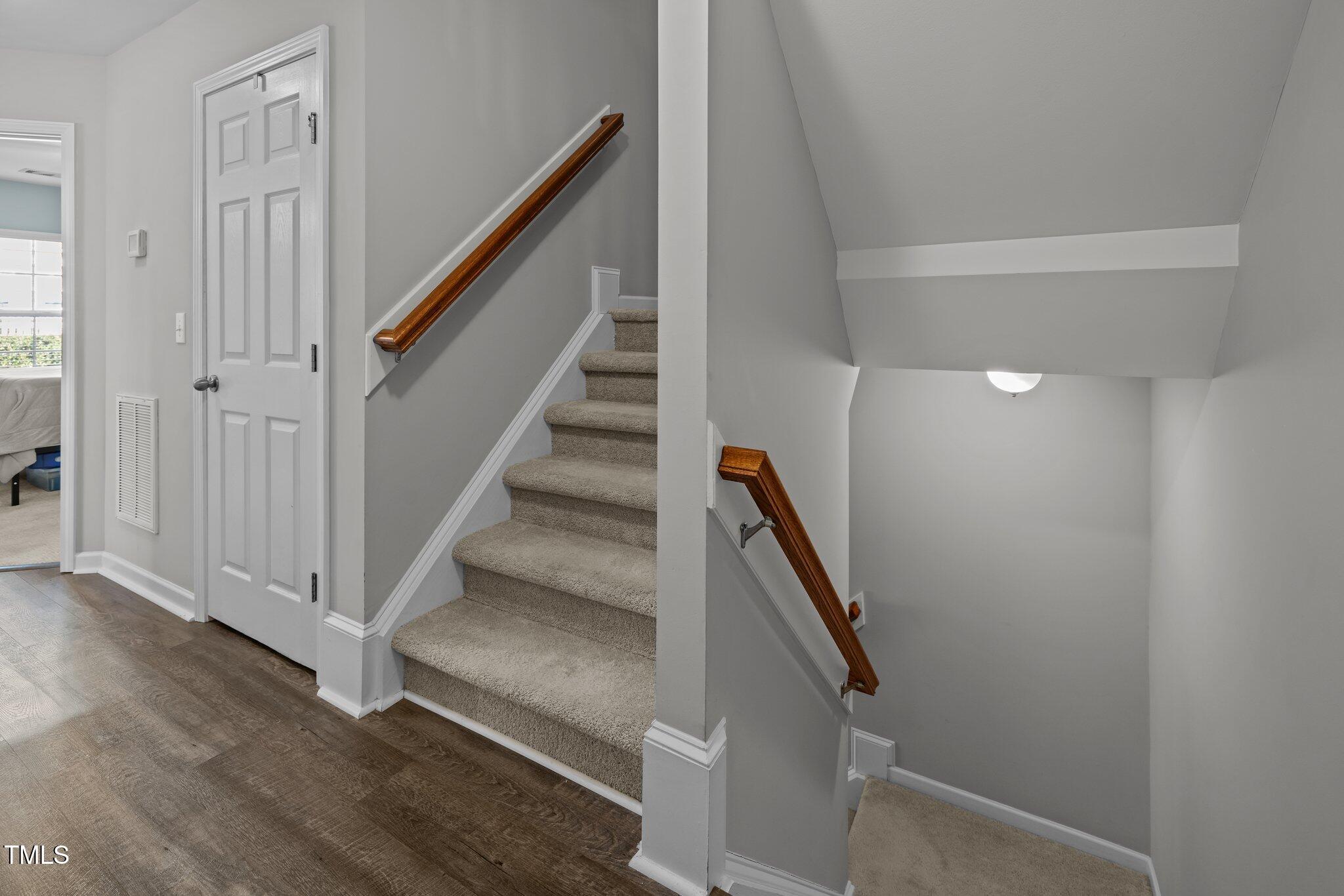 Carpeted townhouse staircase with dark wood handrails, gray walls, and a paneled door.