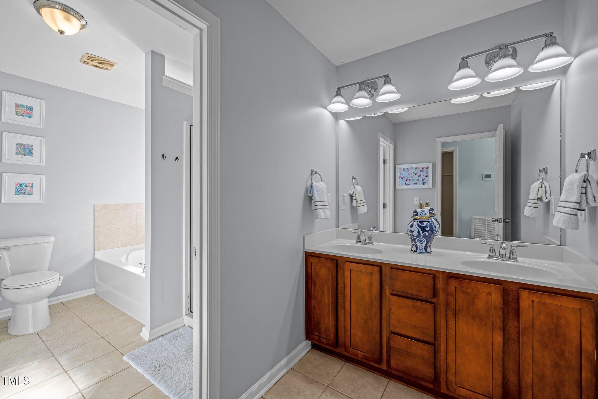 Bathroom with a long double-sink wood vanity, large mirror, and an adjacent tub and toilet.