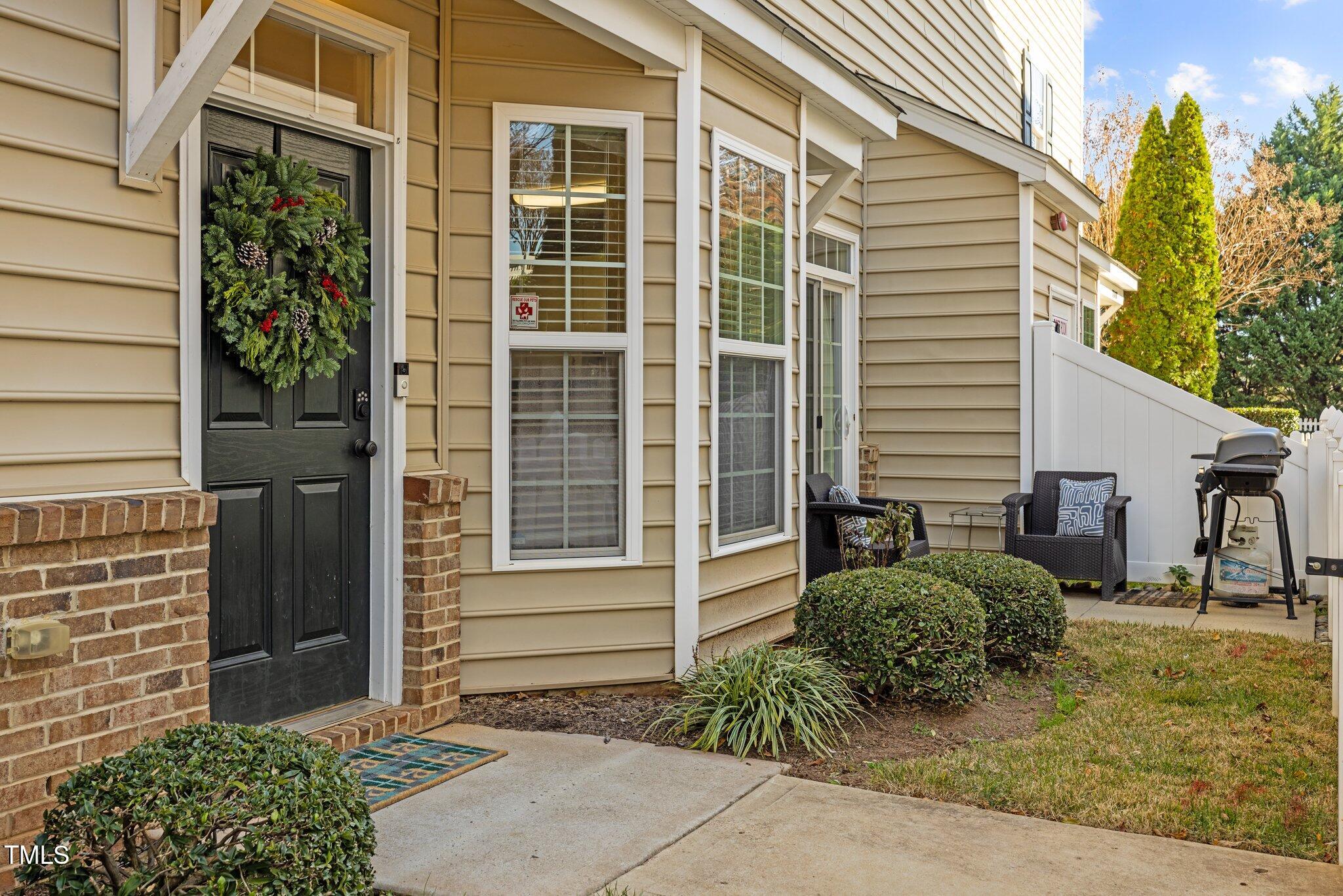 Townhouse entrance with a wreath-covered black door, brick accents, and a furnished patio.