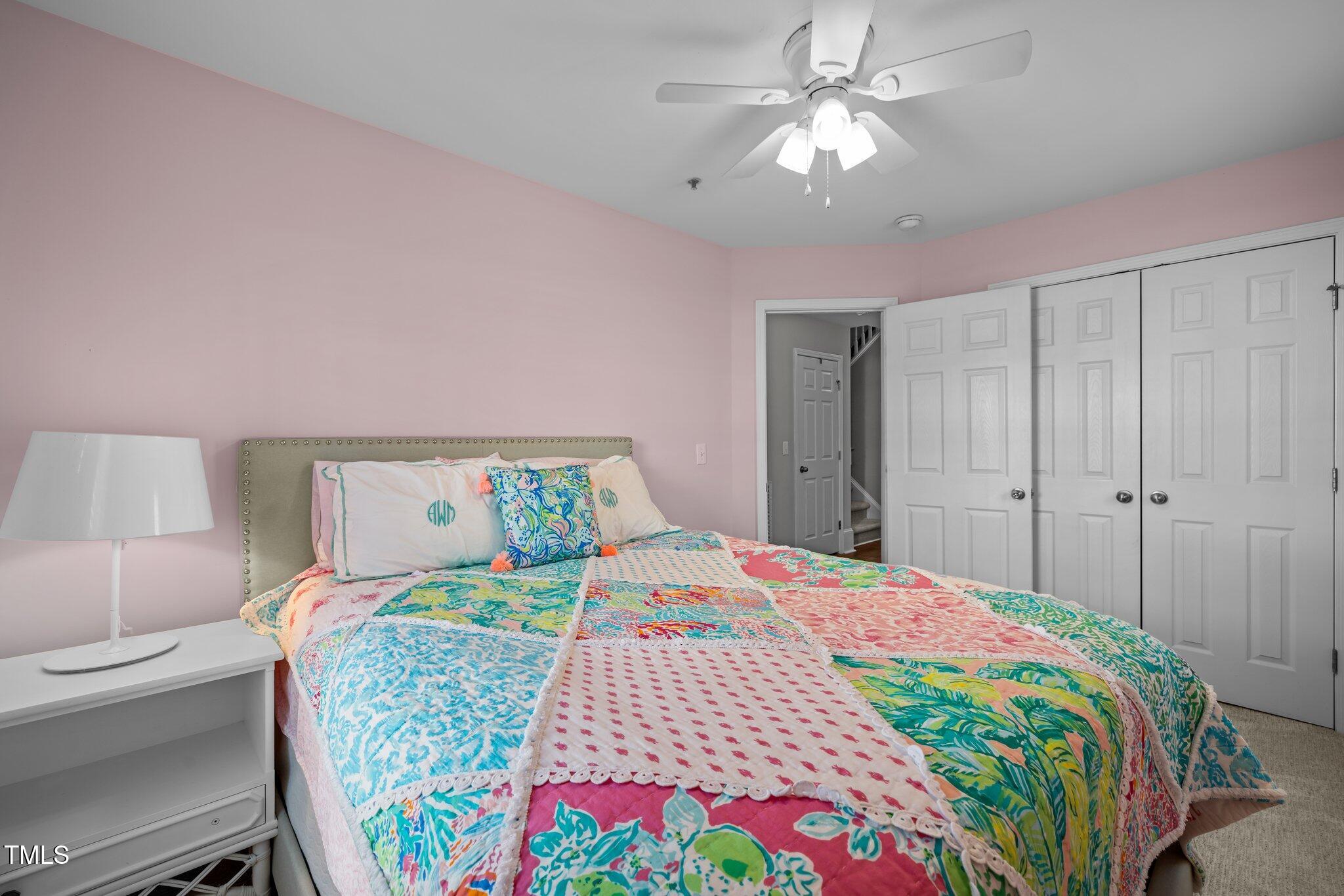 Bedroom with a colorful patchwork quilt, pale pink walls, and white closet doors.