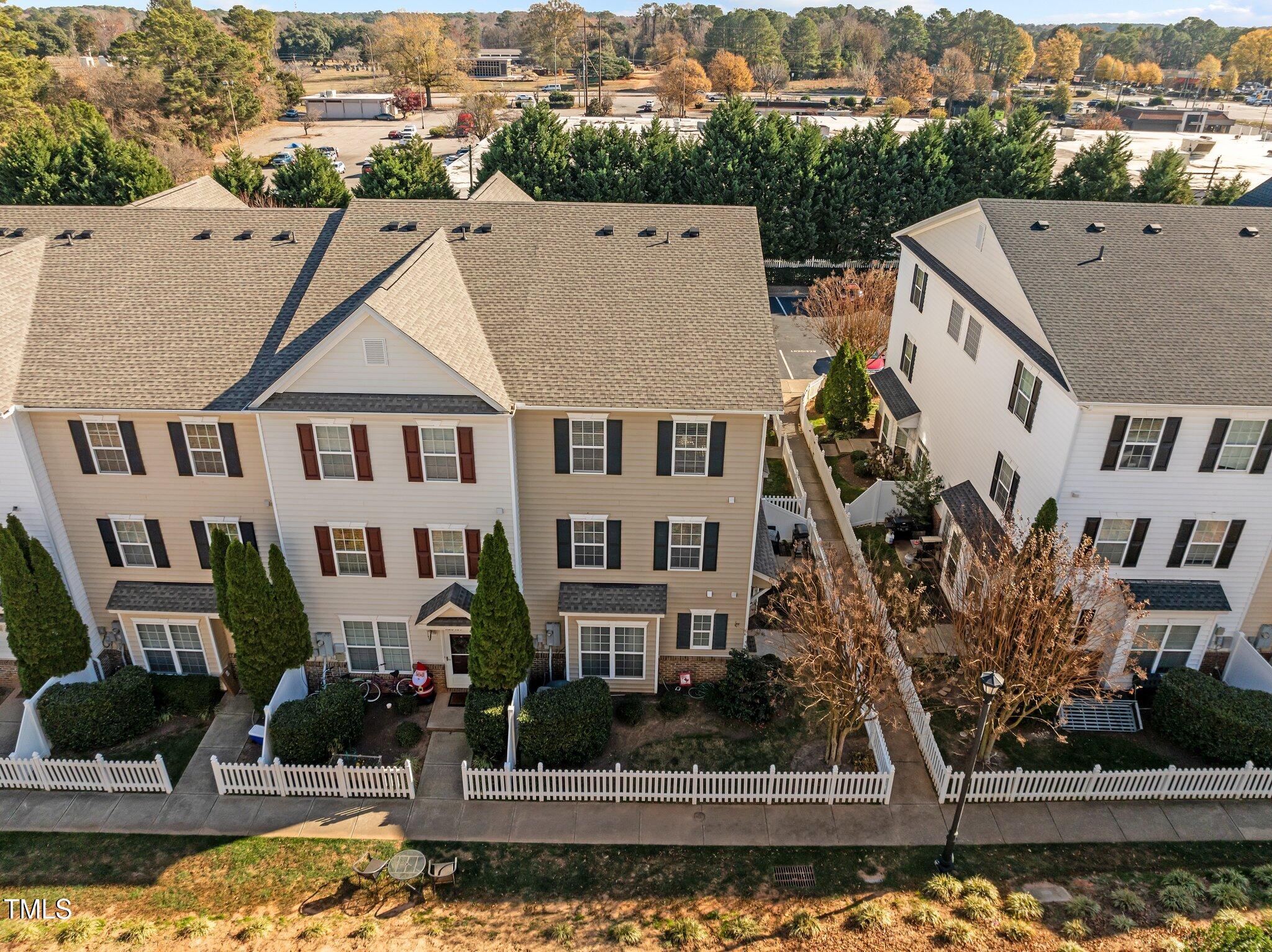 Aerial view of attached townhomes with fenced yards and autumn trees behind them.
