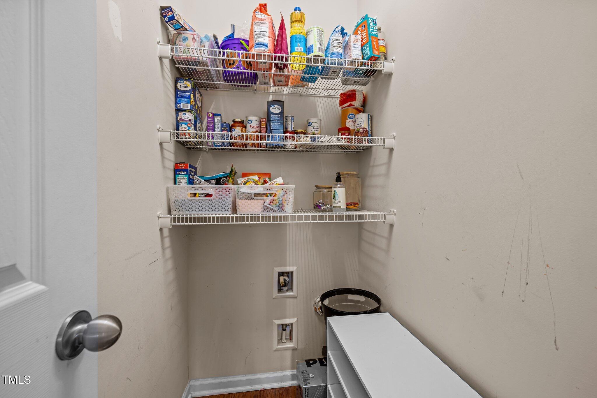 Walk-in pantry with stocked wire shelves, storage baskets, and washer and dryer hookups.