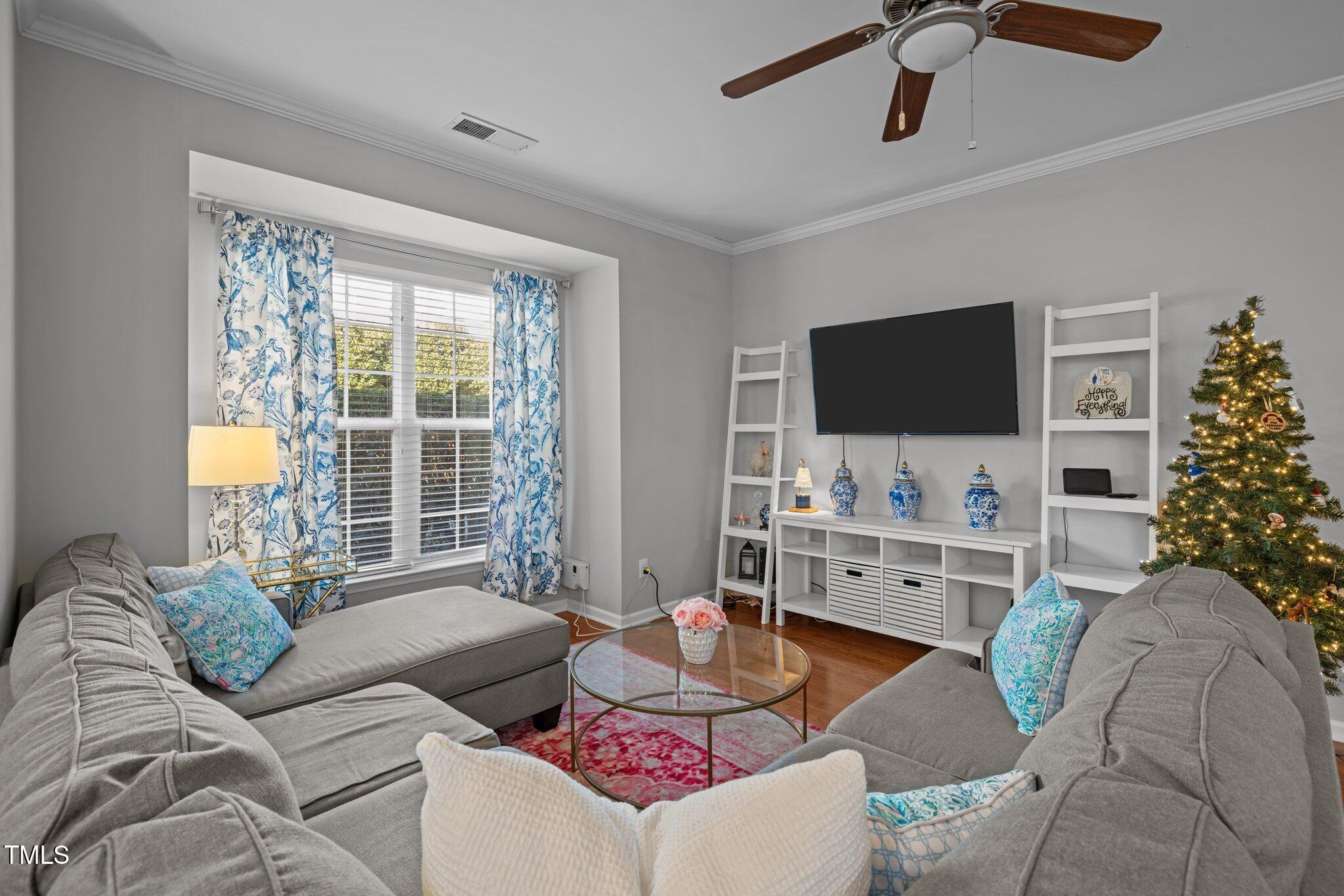 Living room with gray sectional sofas, blue floral curtains, white shelving, and a decorated Christmas tree.