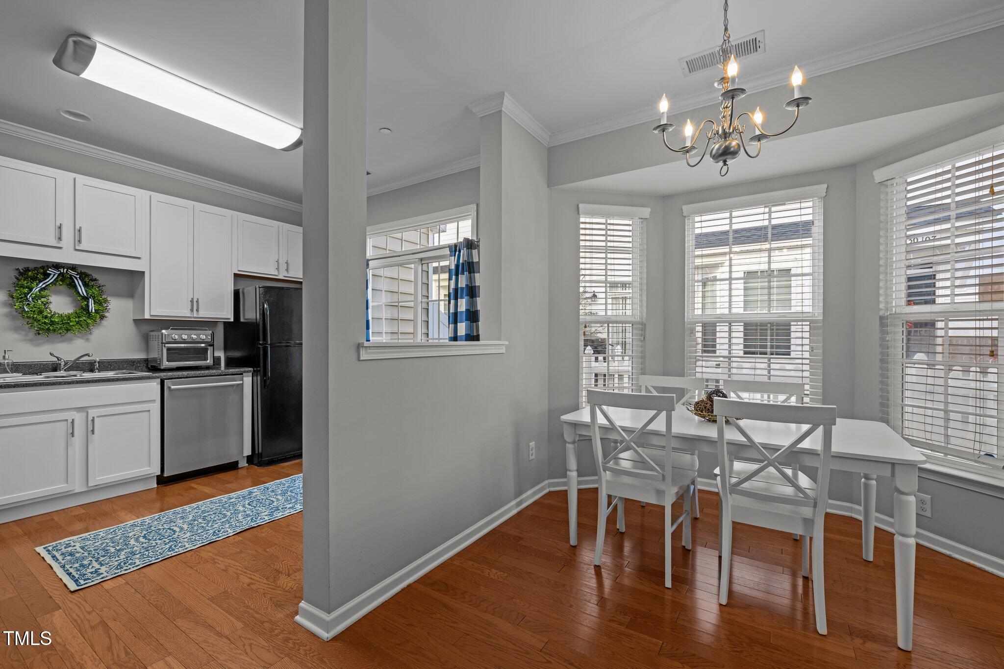 Kitchen and dining area with white cabinetry, hardwood floors, and a table beside large windows.
