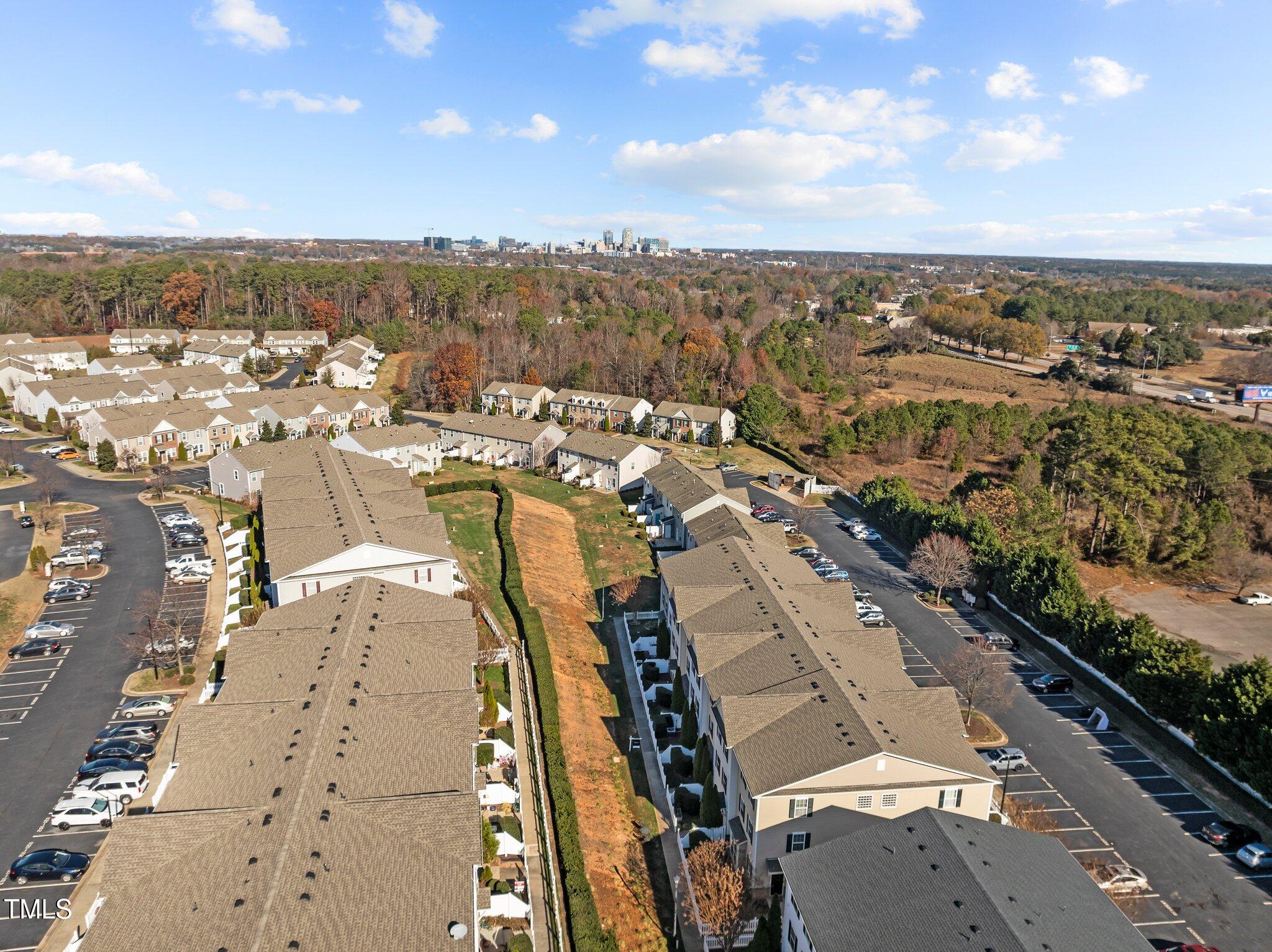 Aerial view of a residential community with parking lots, wooded surroundings, and a distant skyline.