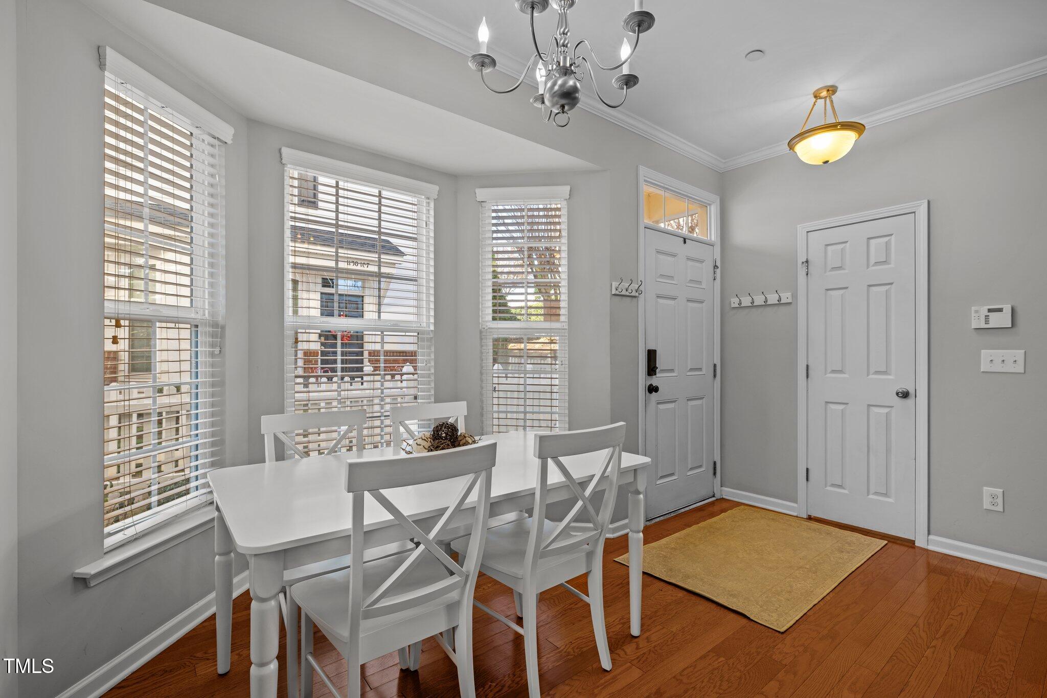 Dining area with a white table and chairs beside tall windows and the front entry.