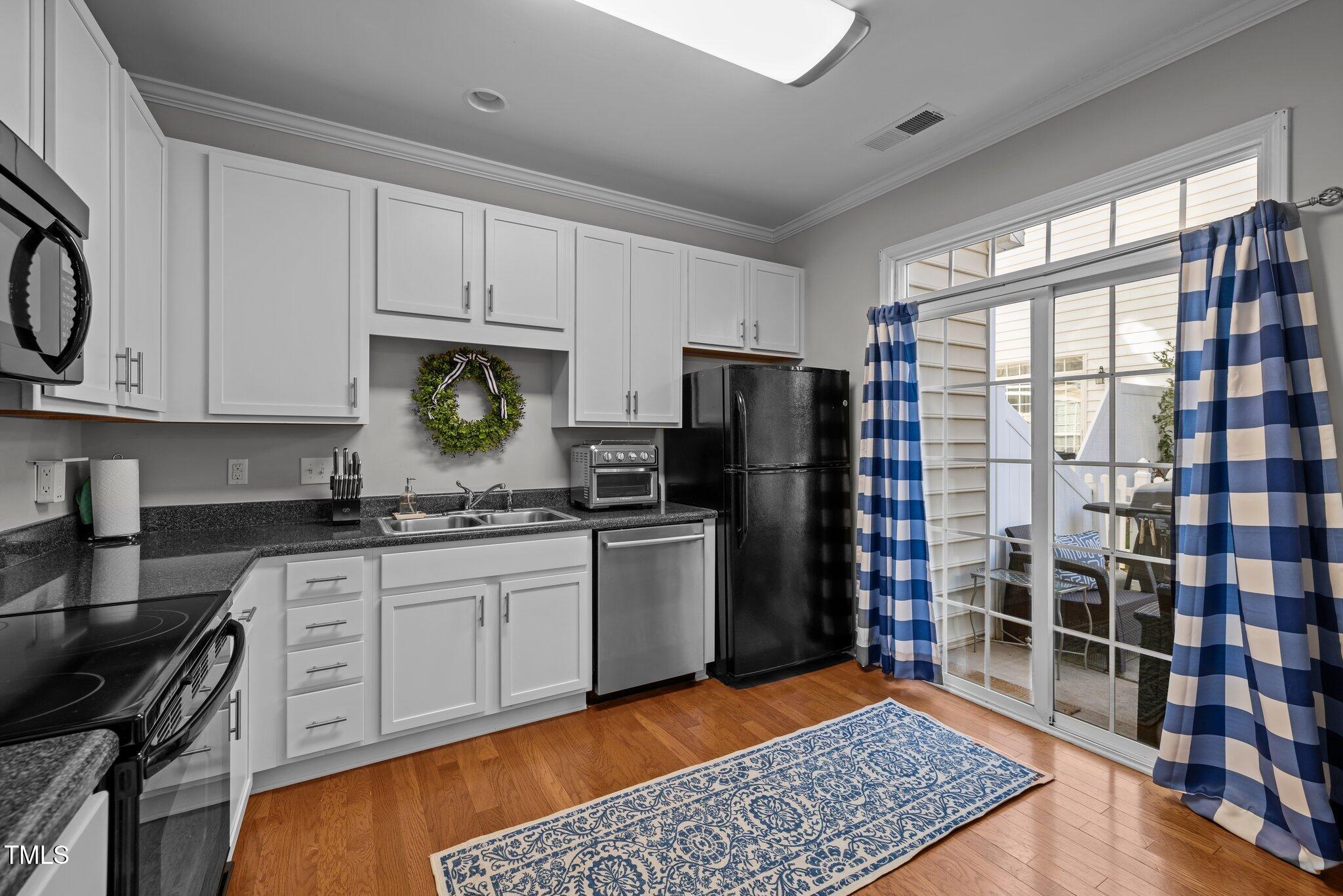 Kitchen with white cabinetry, dark countertops, hardwood floors, and a sliding glass door to a patio.