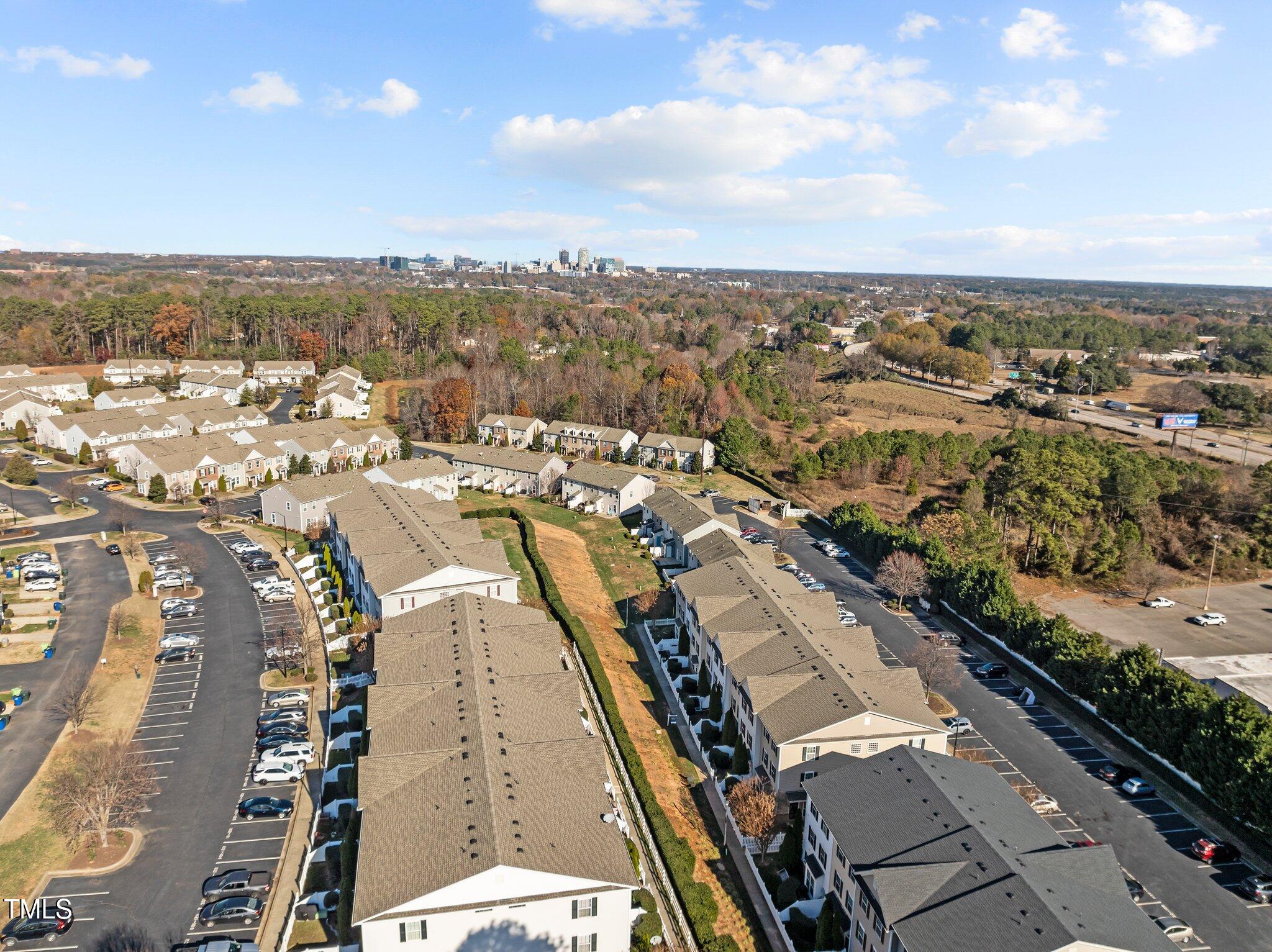 Aerial view of attached homes and parking lots, with the Raleigh skyline in the distance.