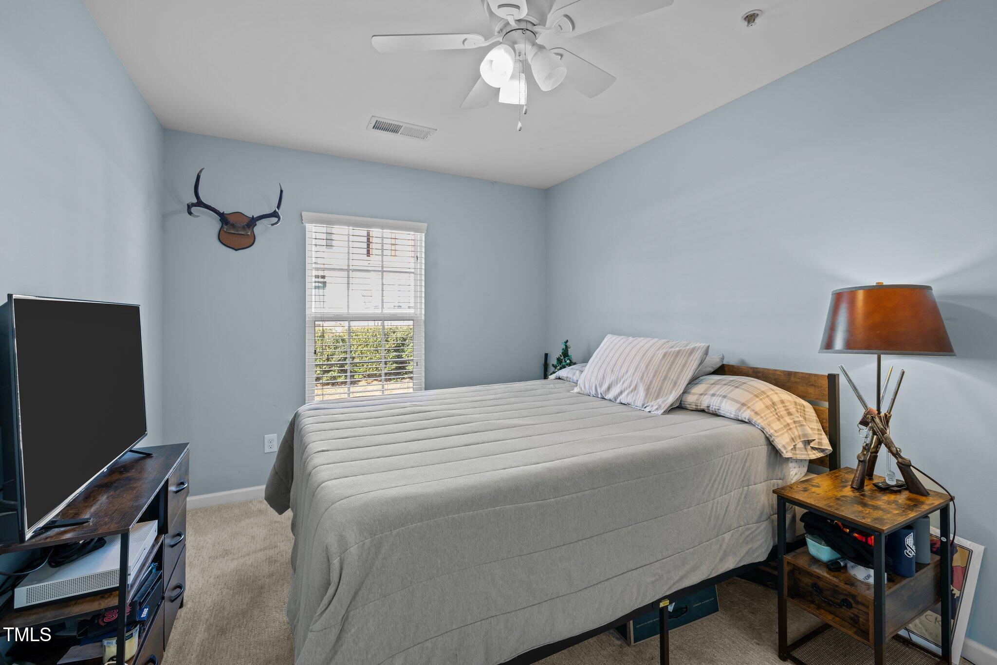 Bedroom with a gray-covered bed, pale blue walls, and mounted antler decoration beside the window.