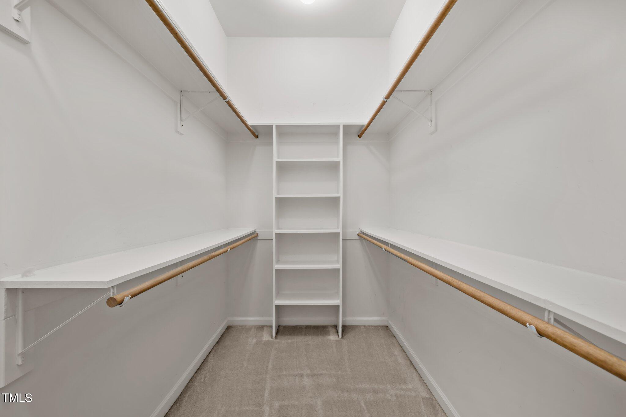 Walk-in closet with built-in shelves, wooden hanging rods, and carpeted floor.