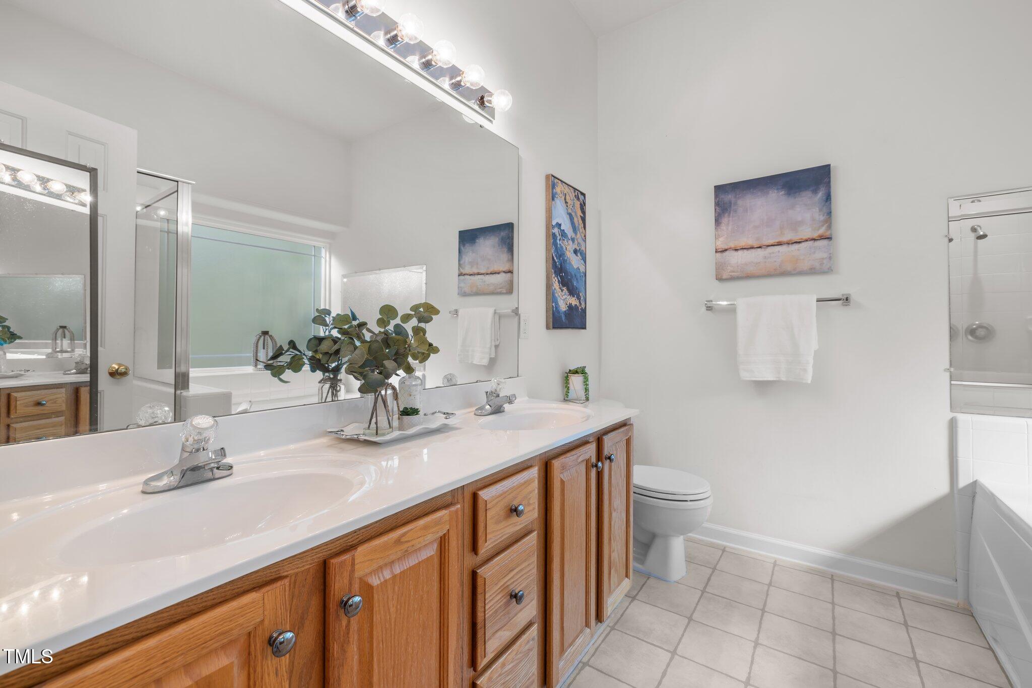 Bathroom with a long double-sink vanity, warm wood cabinets, and a tub-shower enclosure.