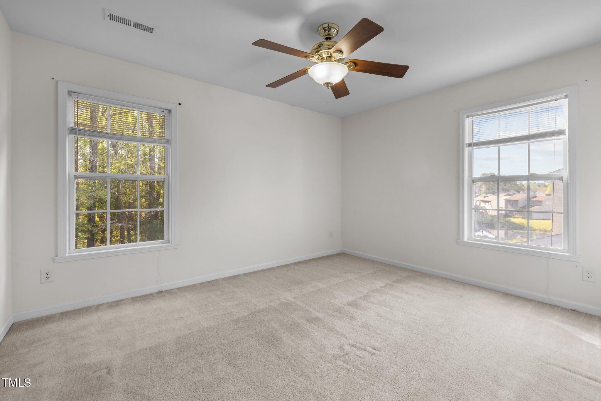 Empty carpeted bedroom with two windows and a wood-bladed ceiling fan.