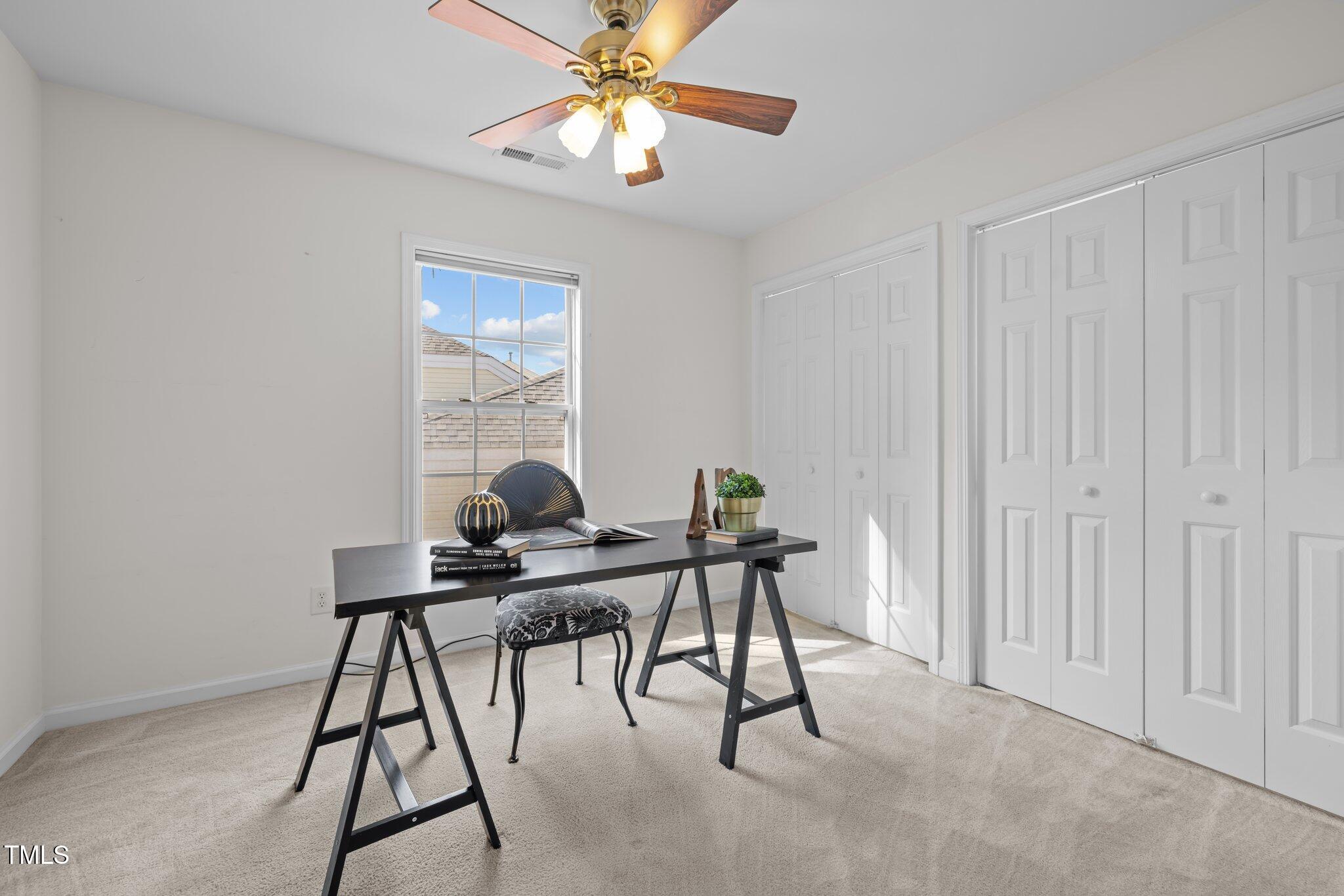 Bright home office with a black desk, patterned chair, window, and white closet doors.