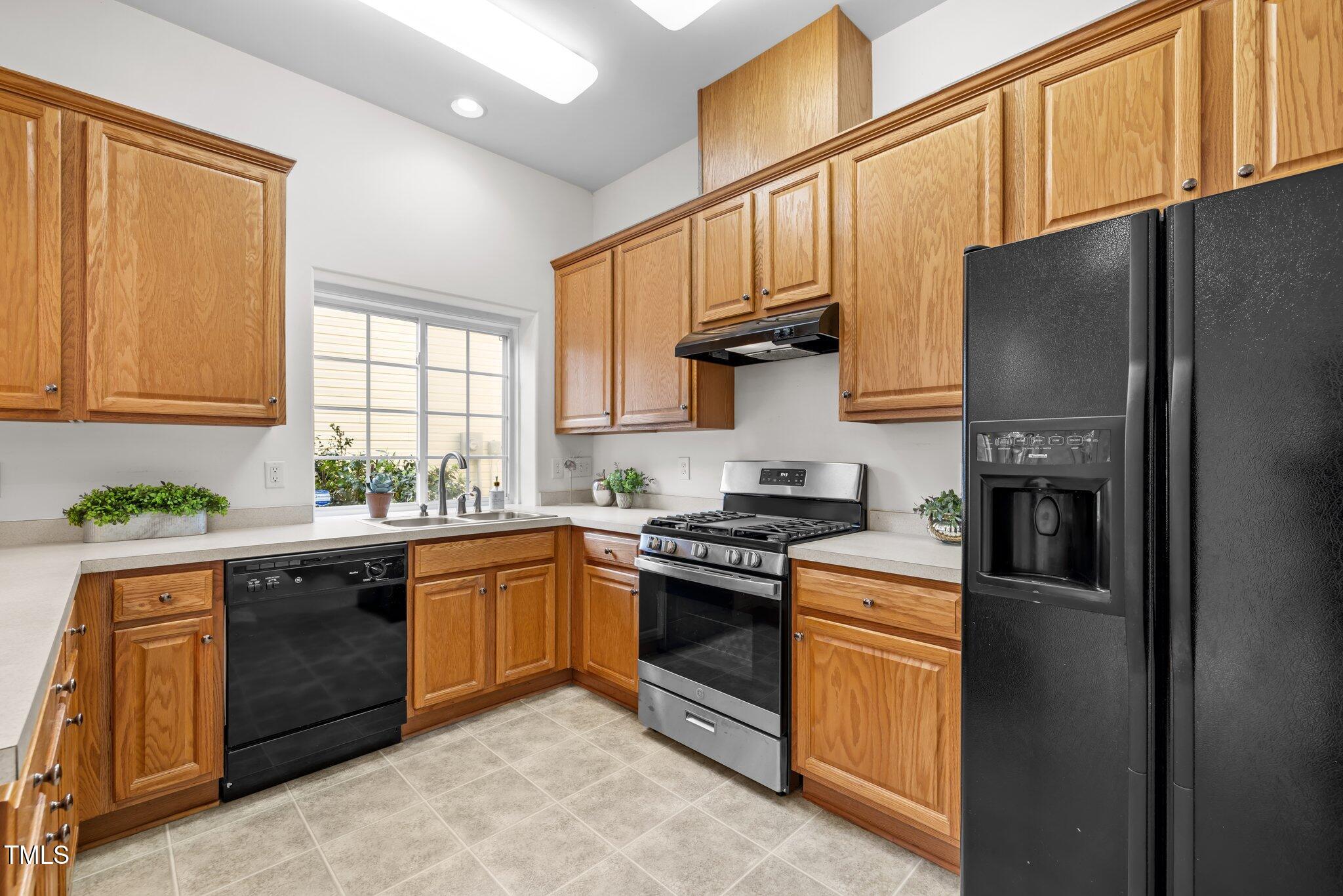 Kitchen with honey-colored wood cabinets, a window over the sink, and black and stainless-steel appliances.