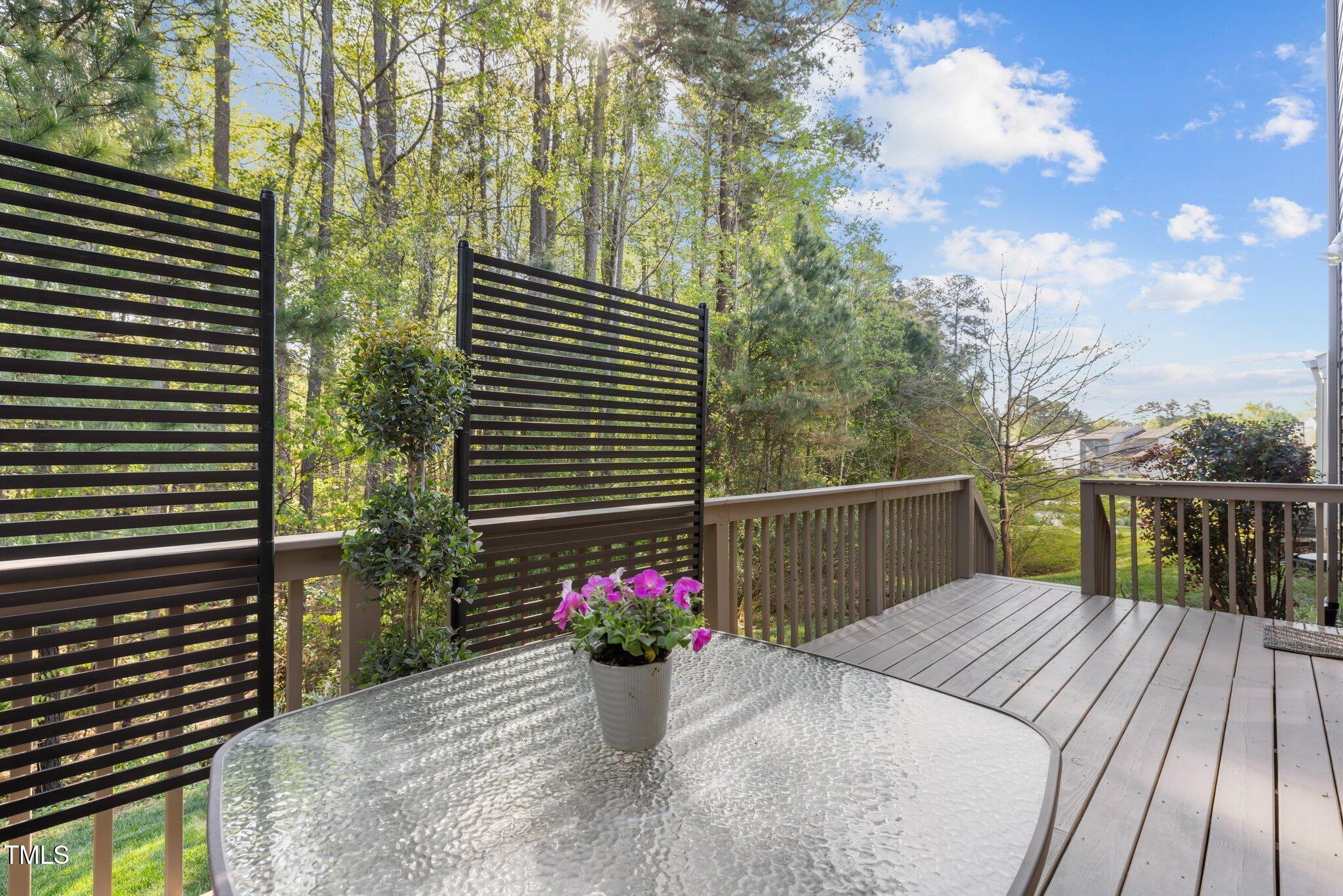 Outdoor deck with dark privacy screens, a glass-top table, and wooded surroundings.