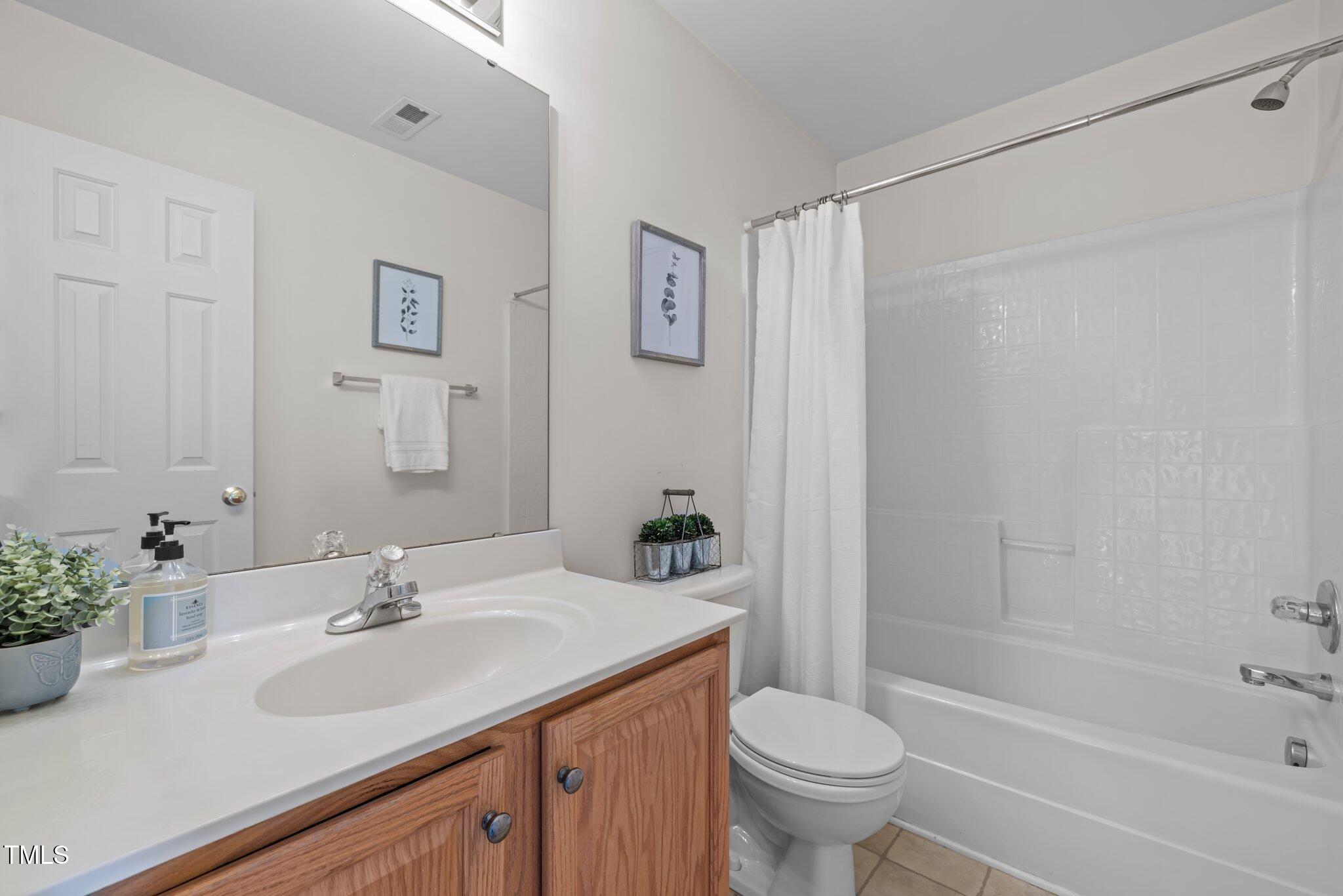 Bathroom with a wood vanity, white sink, toilet, and tiled tub-shower.