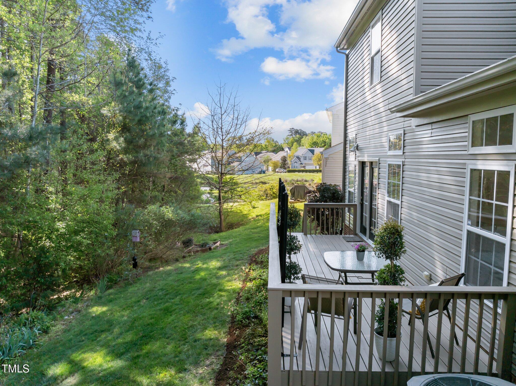 Raised deck beside a gray-sided home overlooks a wooded, sloping yard.