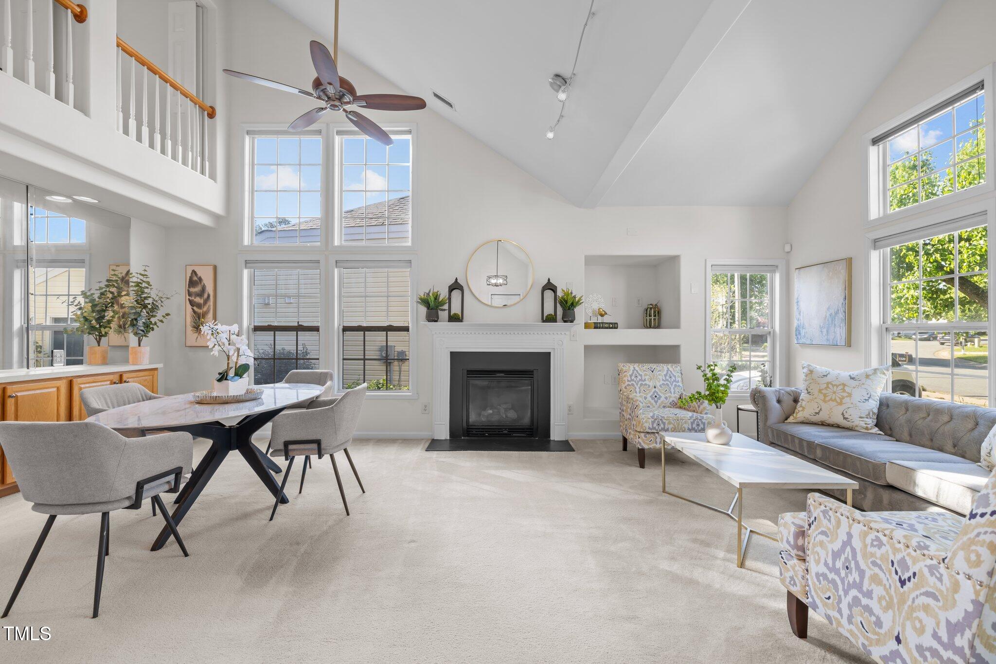 Furnished living room and dining area with vaulted ceiling, large windows, and a central fireplace.