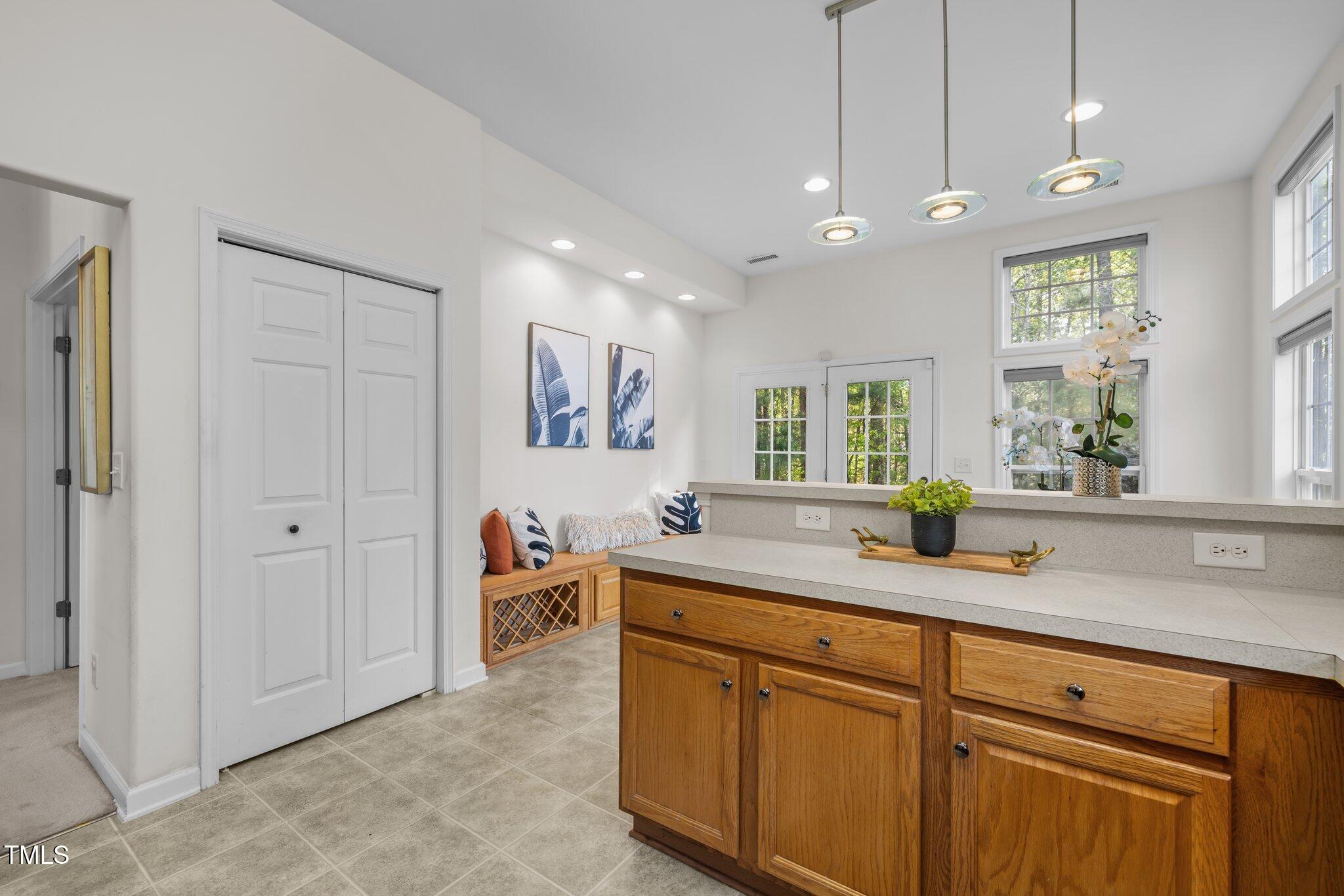 Bright mudroom with a long wood cabinet, countertop, and built-in bench beside glass-paneled doors.